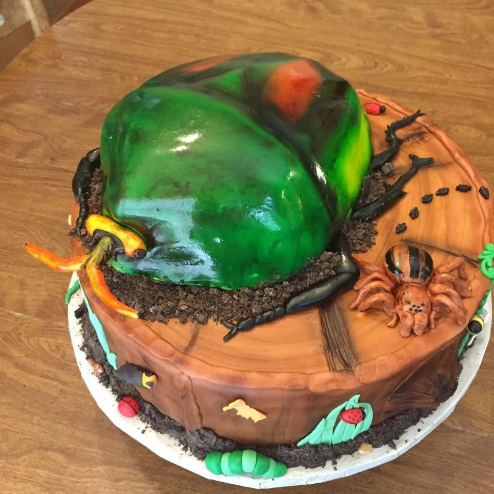 Vibrant beetle sculpted cake on tree stump with detailed edible insects