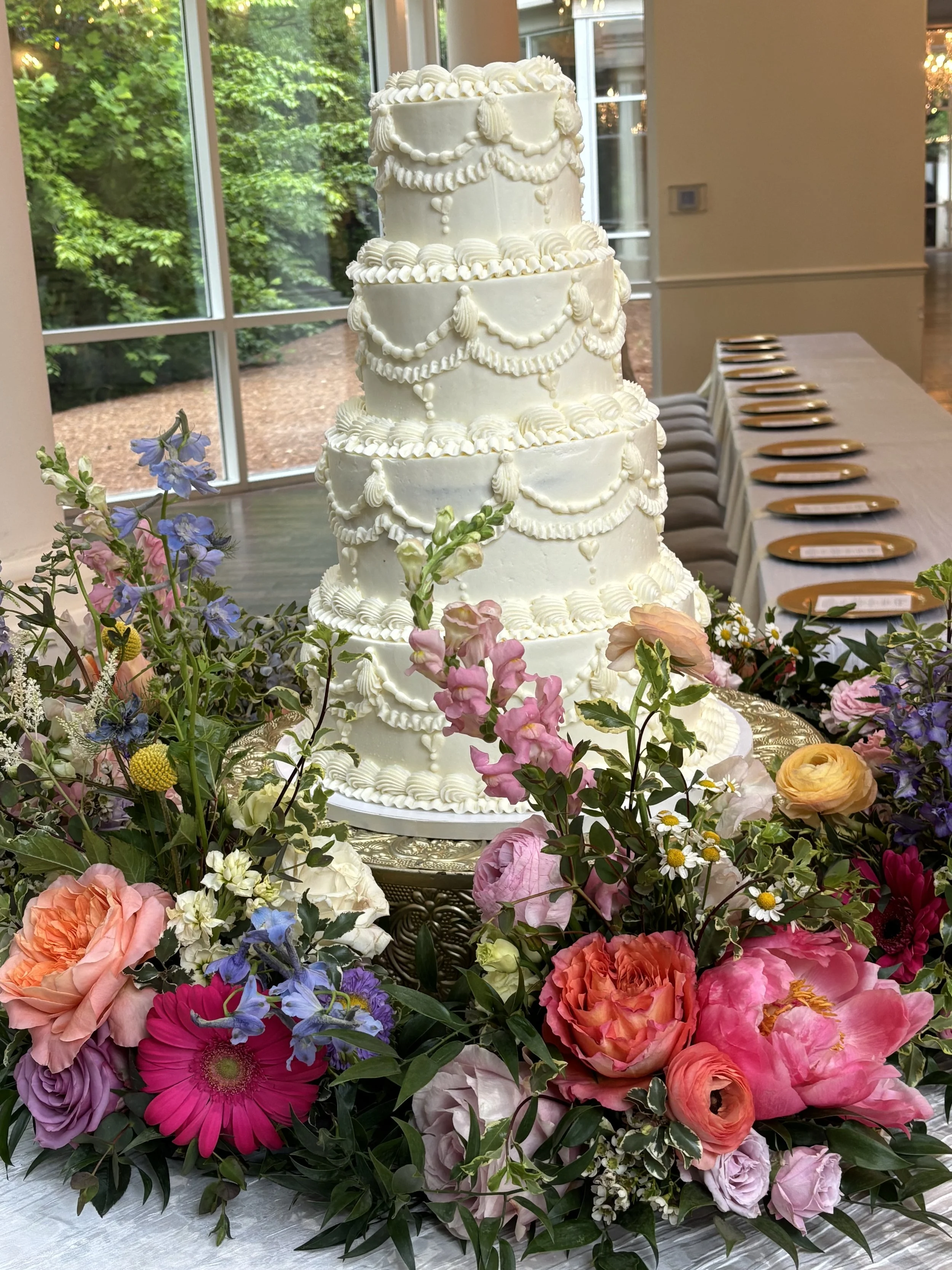 Four tiered buttercream wedding cake with vintage piping surrounded by a cake meadow at Ashton Gardens Atlanta