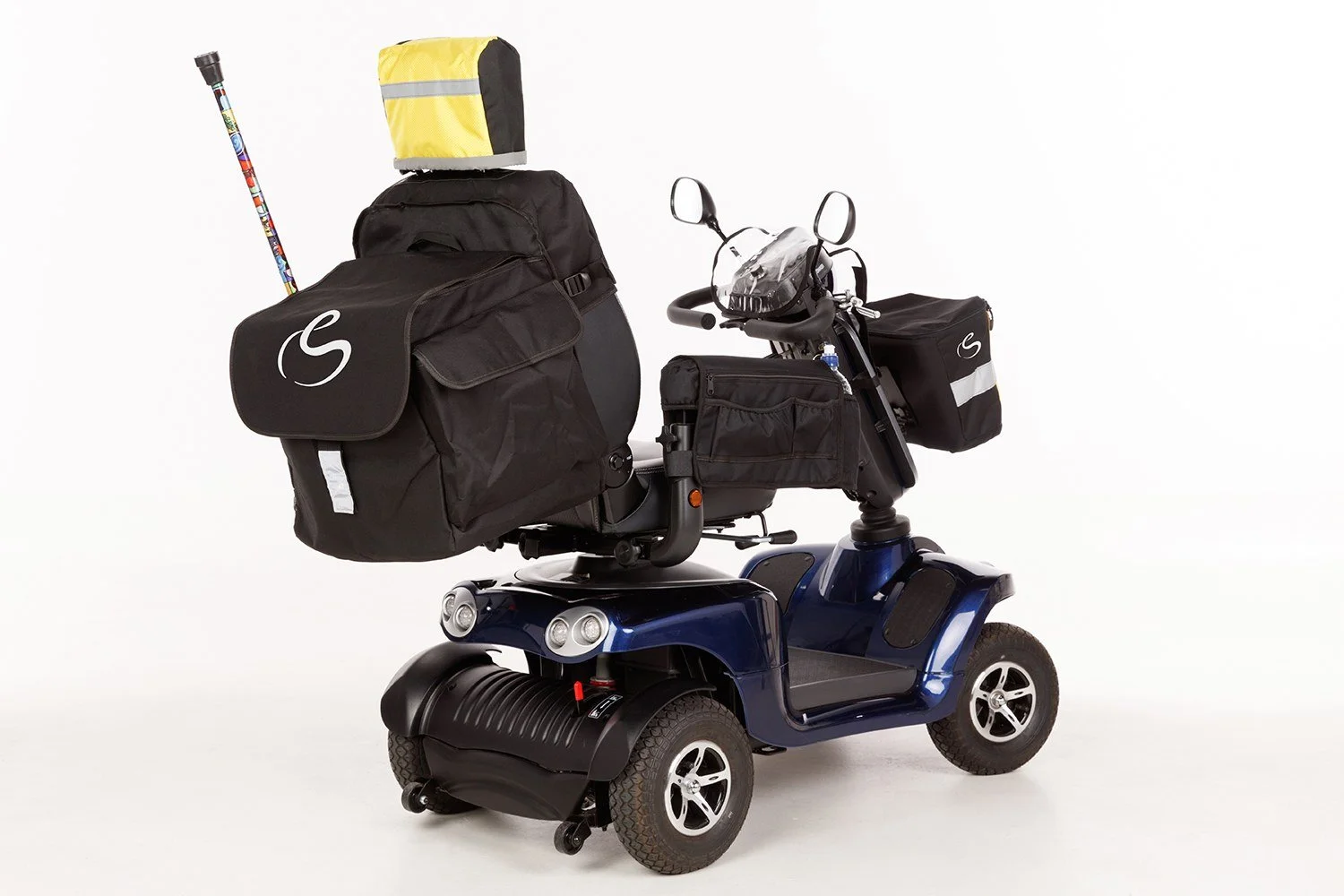 A mobility scooter with multiple bags, a yellow and gray box on top, and a colorful walking stick, set against a plain white background.