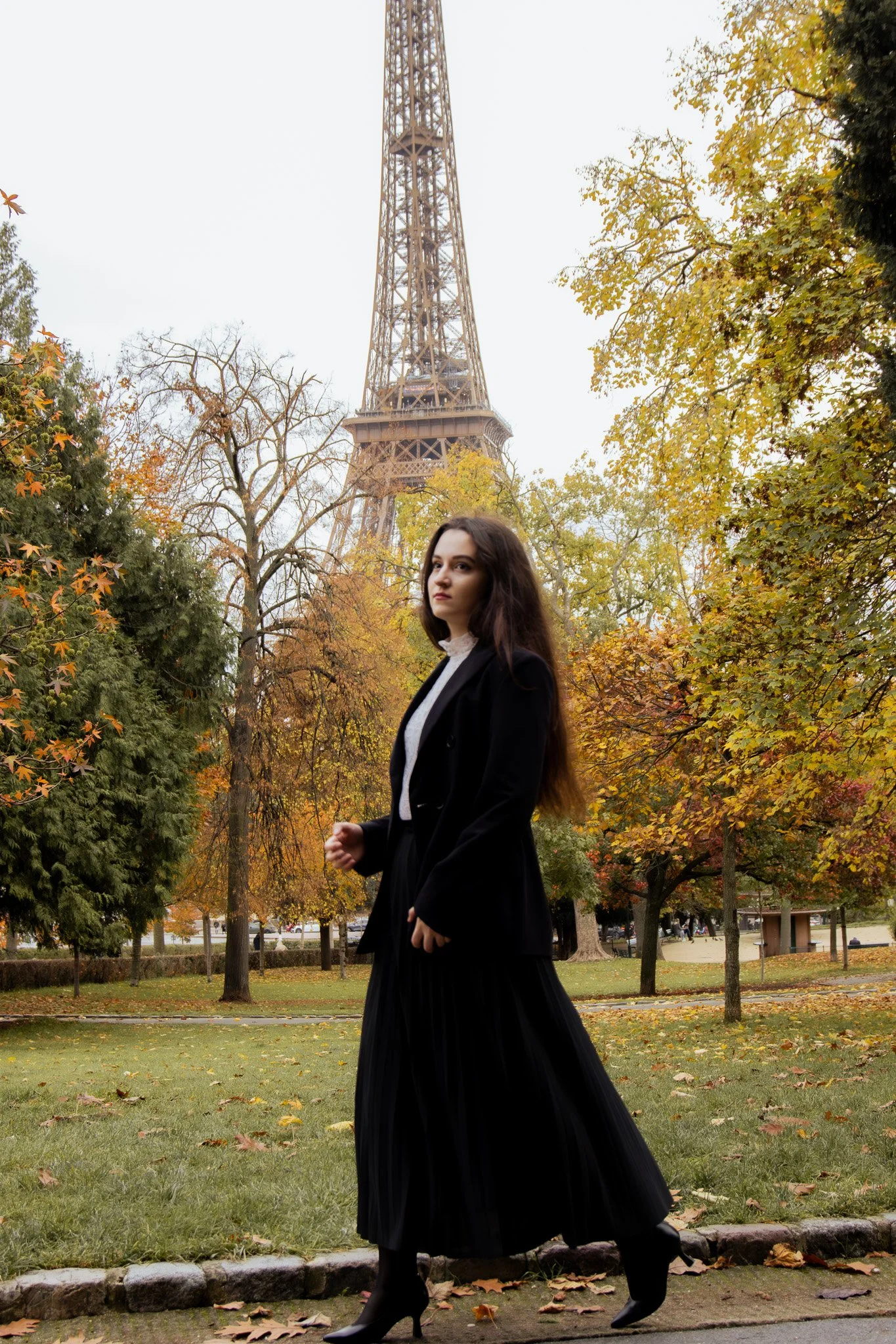 A woman walking in a park with autumn foliage, the Eiffel Tower in the background.