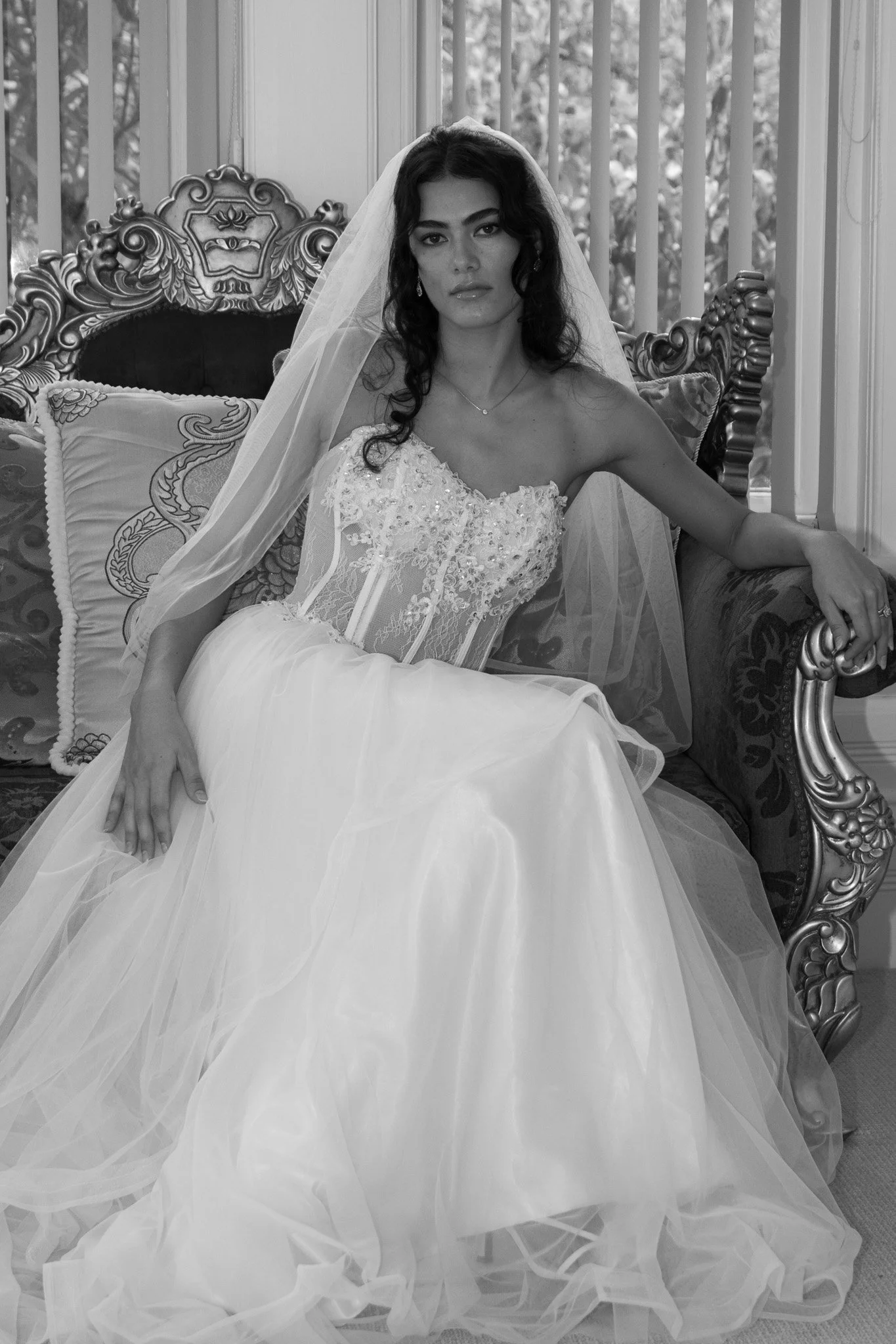 Black and white photo of a woman in wedding dress sitting on ornate sofa.