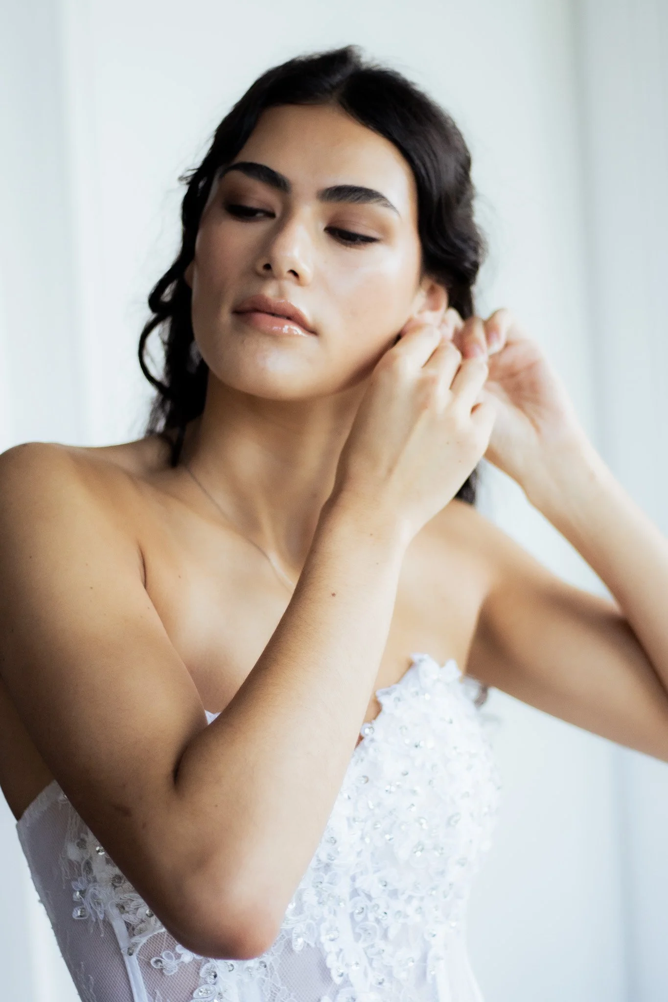 A woman in a wedding dress is putting on earrings.