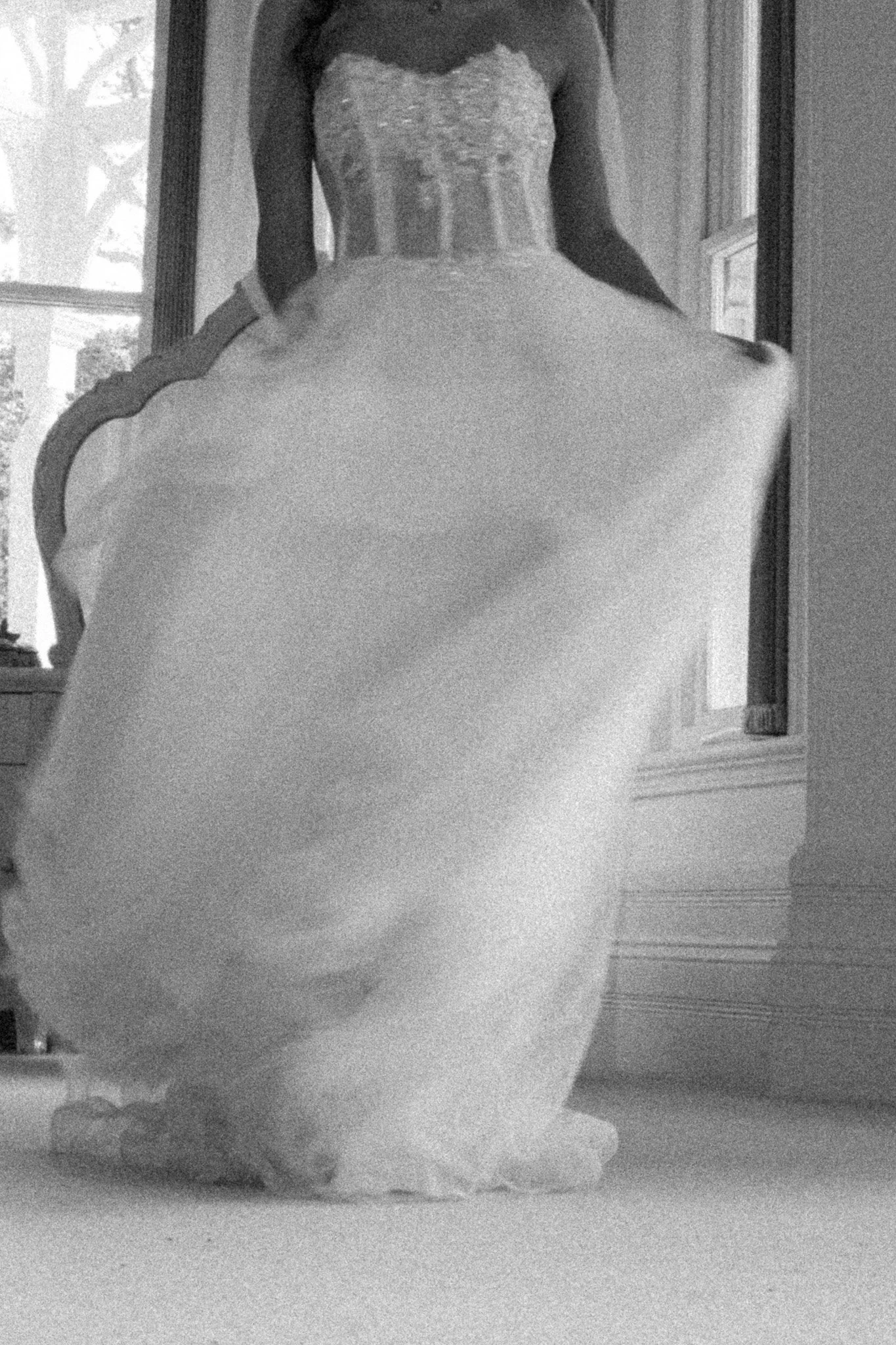 A woman standing in front of a mirror in a dress with a fitted bodice and full skirt, captured in black and white.