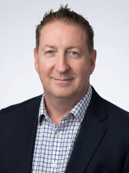 A middle-aged man with short, light brown hair, wearing a navy blazer and a blue and white checkered dress shirt, smiling slightly against a plain white background.