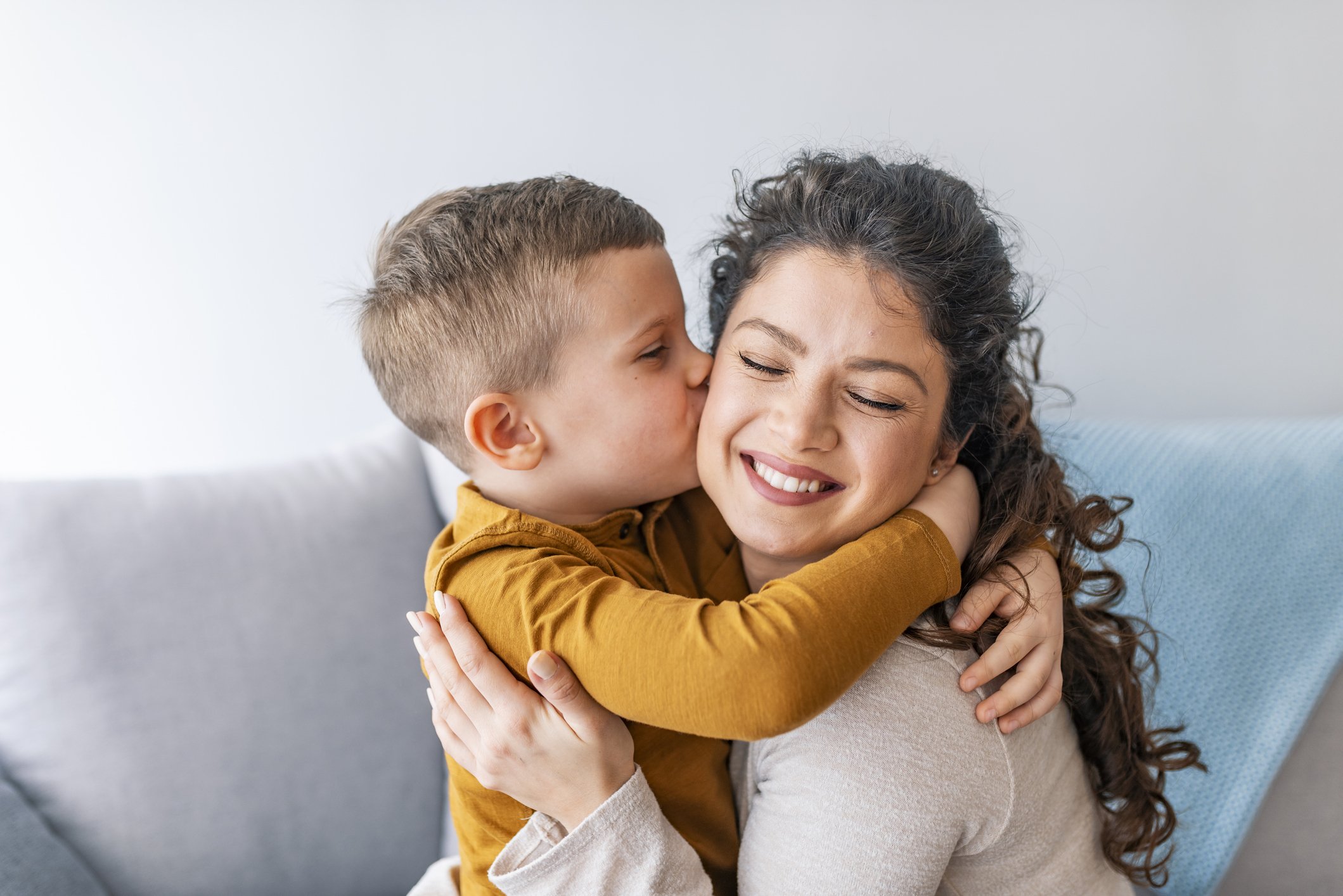 A young boy giving a woman a hug and kissing her cheek, both smiling.