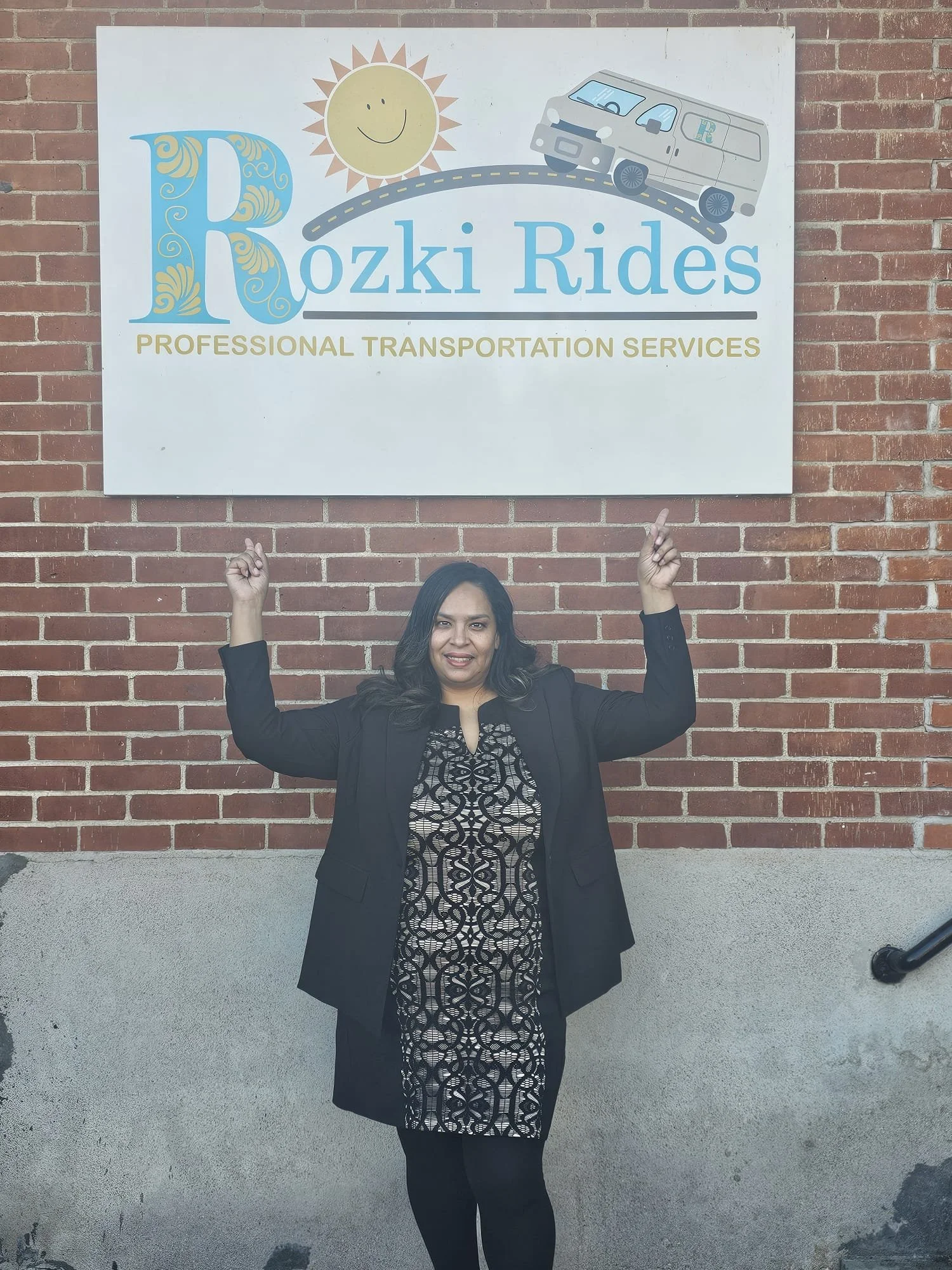 Jessika Rozki standing in front of a brick wall, pointing up, with a sign that reads 'Rozki Rides' and 'Professional Transportation Services,' featuring a sun, a road, and a van illustration.