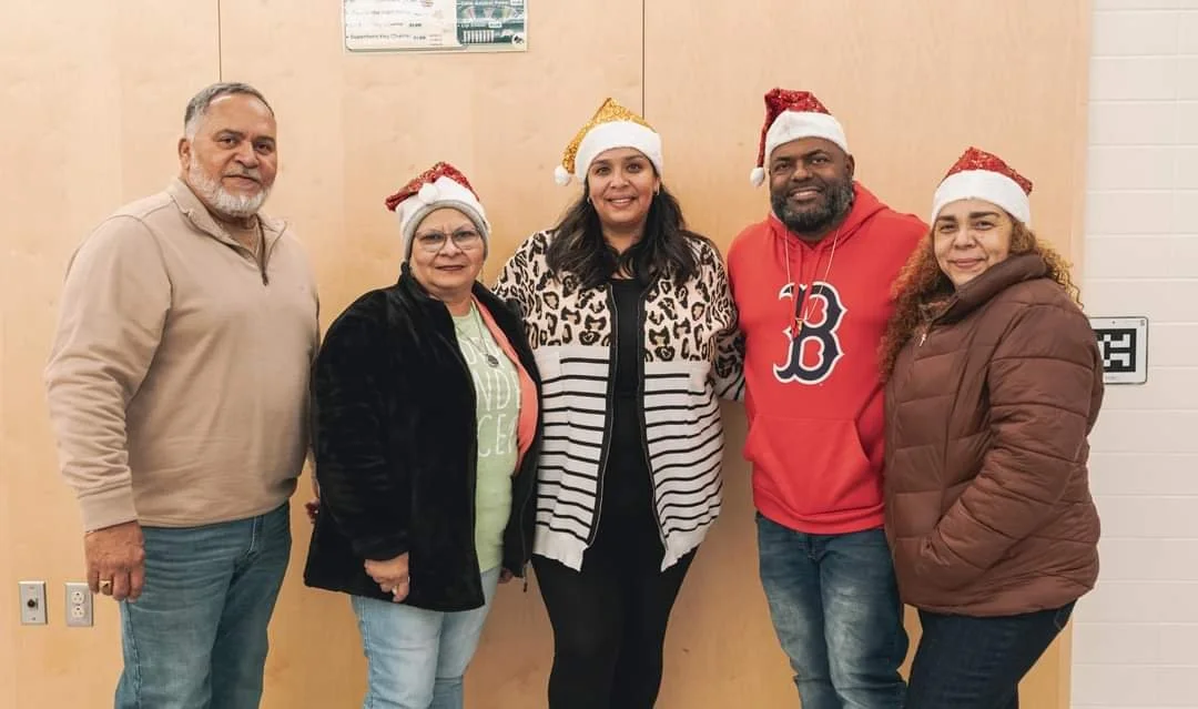 Xmas Dinner together wearing Christmas hats, posing in front of a wooden wall.