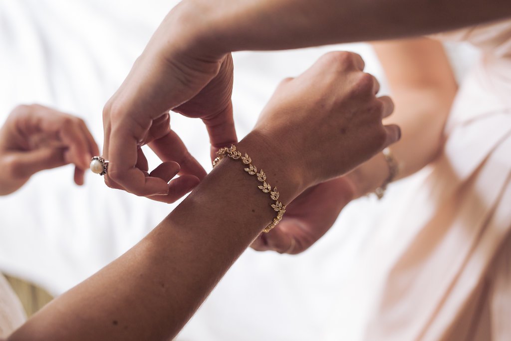 Person fastening a decorative bracelet on another's wrist, with blurred background.