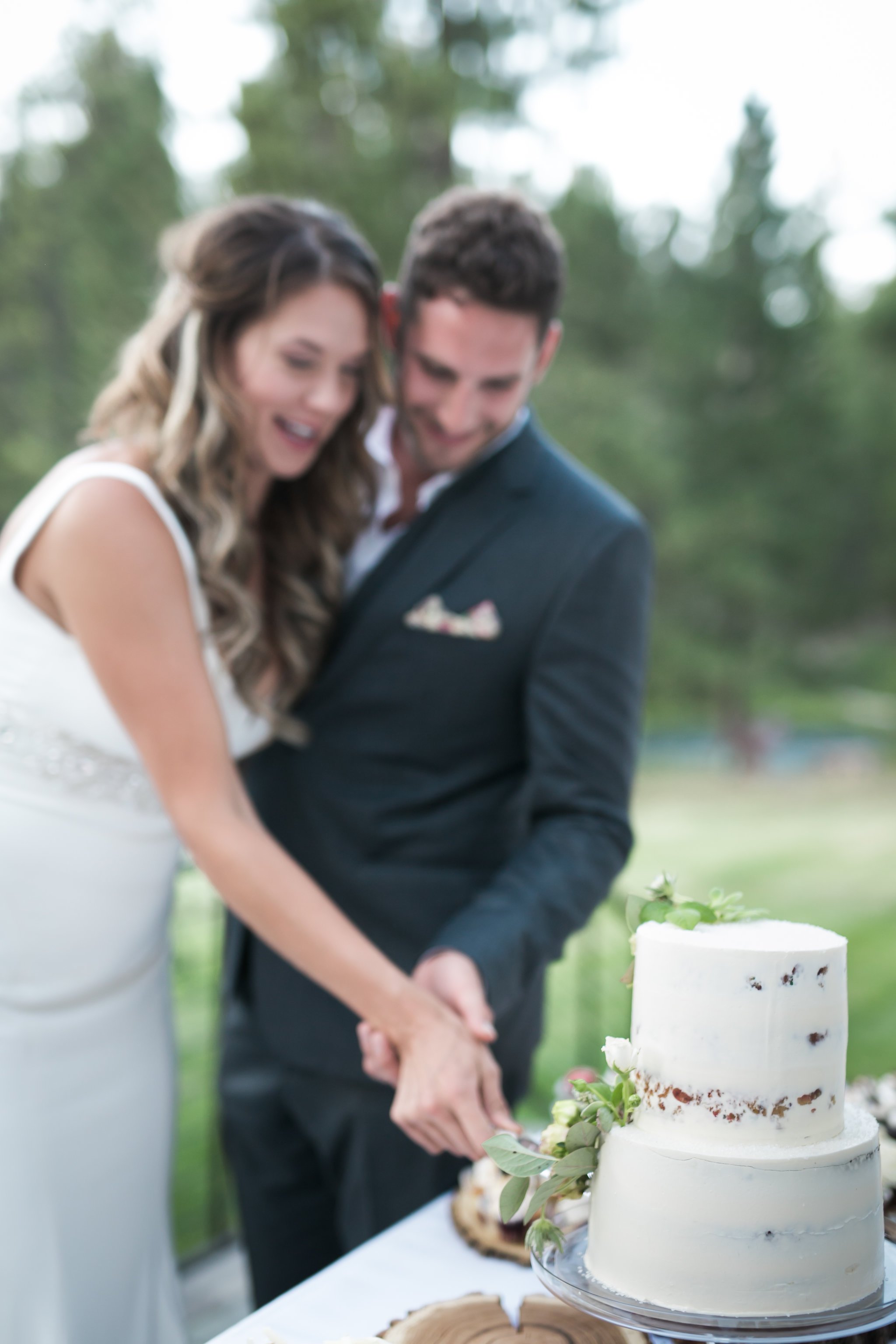 Bride and groom cutting a white wedding cake outdoors.