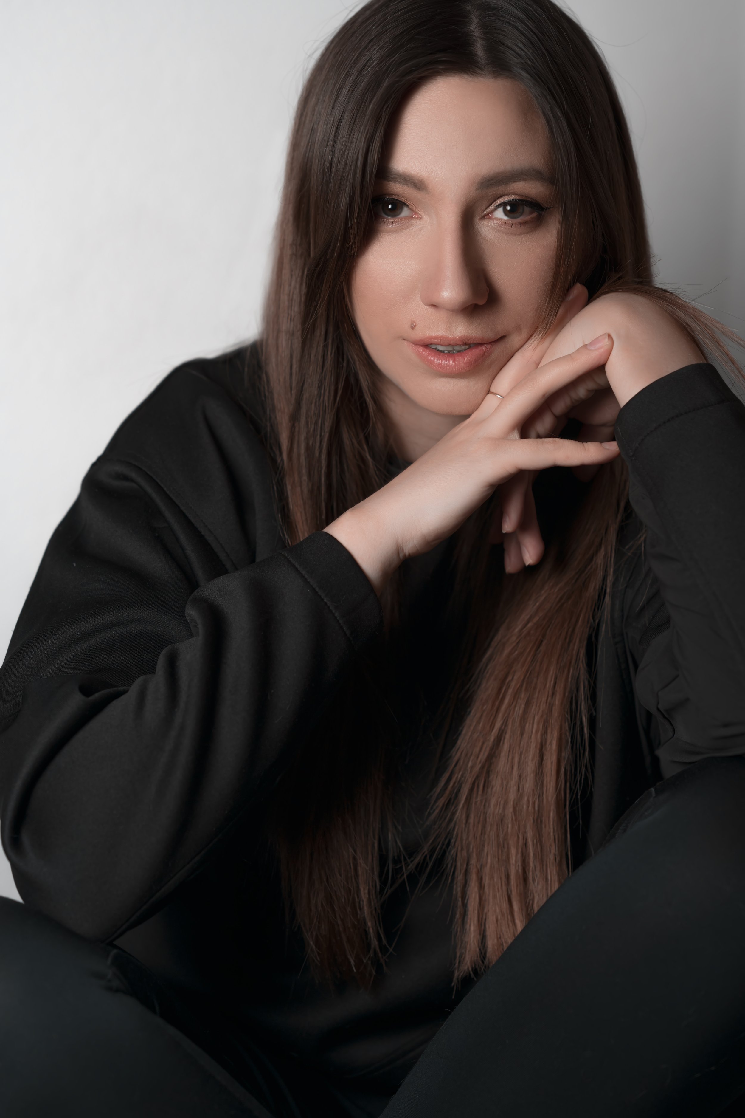 Woman with long brown hair resting chin on hands, wearing black clothing.