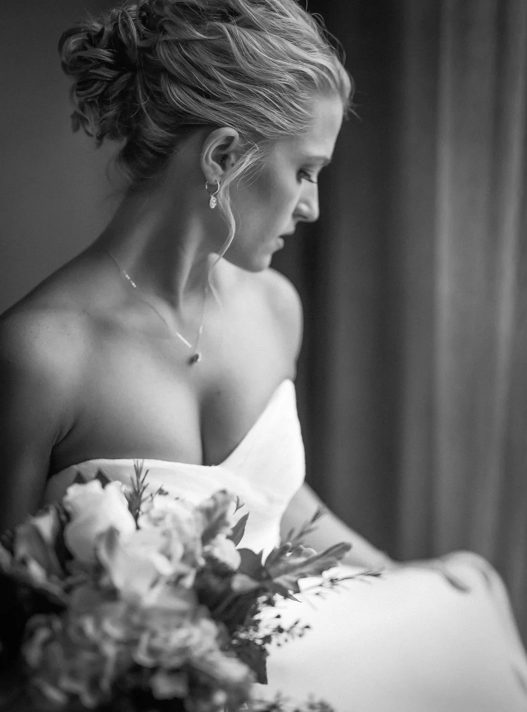 Black and white photo of a woman in a strapless dress holding a bouquet, facing sideways.