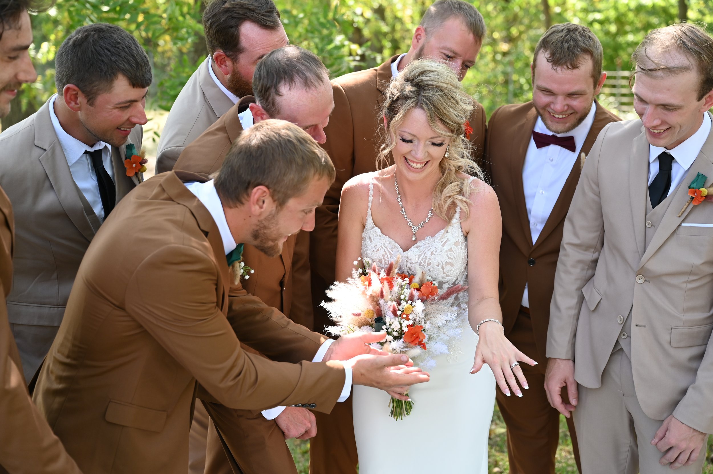 Bride showing ring to groomsmen outdoors at wedding