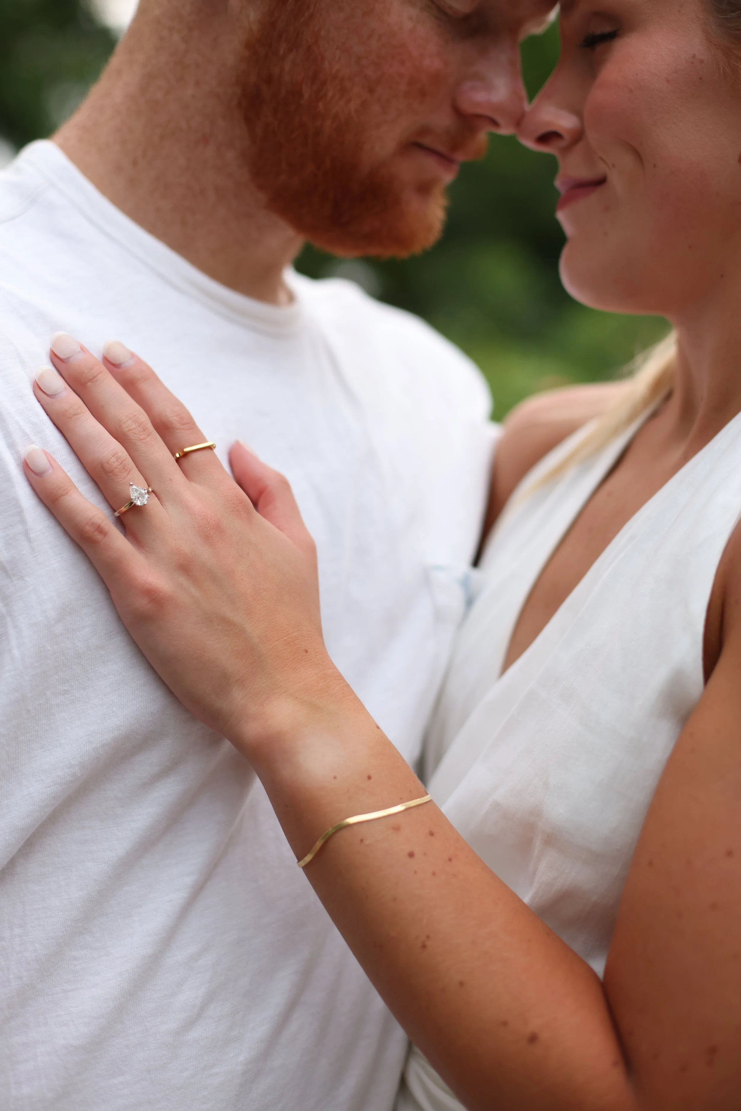 Close-up of a couple embracing with a focus on woman's engagement ring on man's chest.
