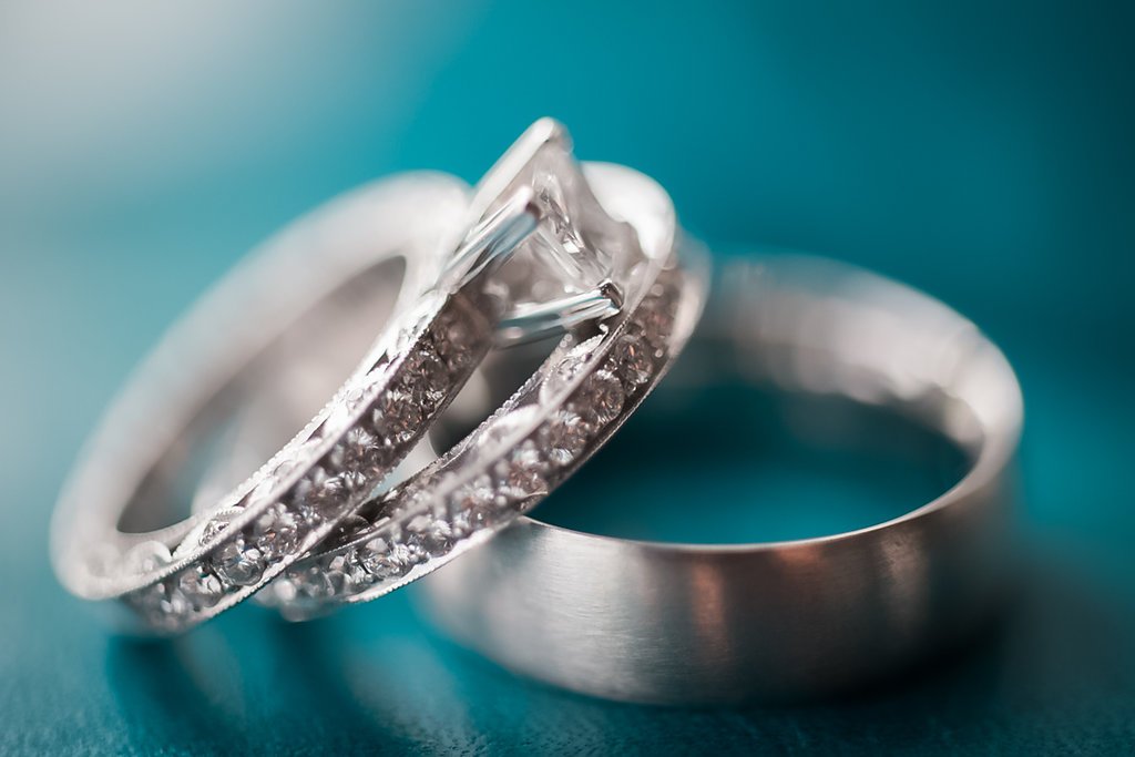 Close-up of silver wedding rings with diamond accents, placed on a teal background.