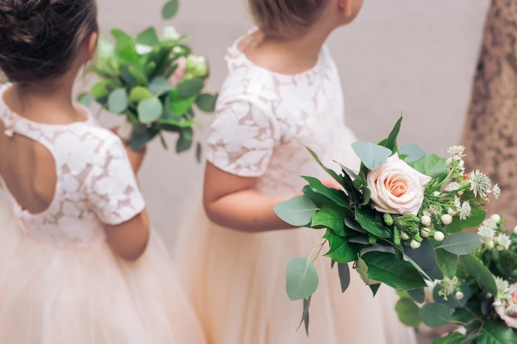 Two young flower girls with floral bouquets wearing matching lace dresses.
