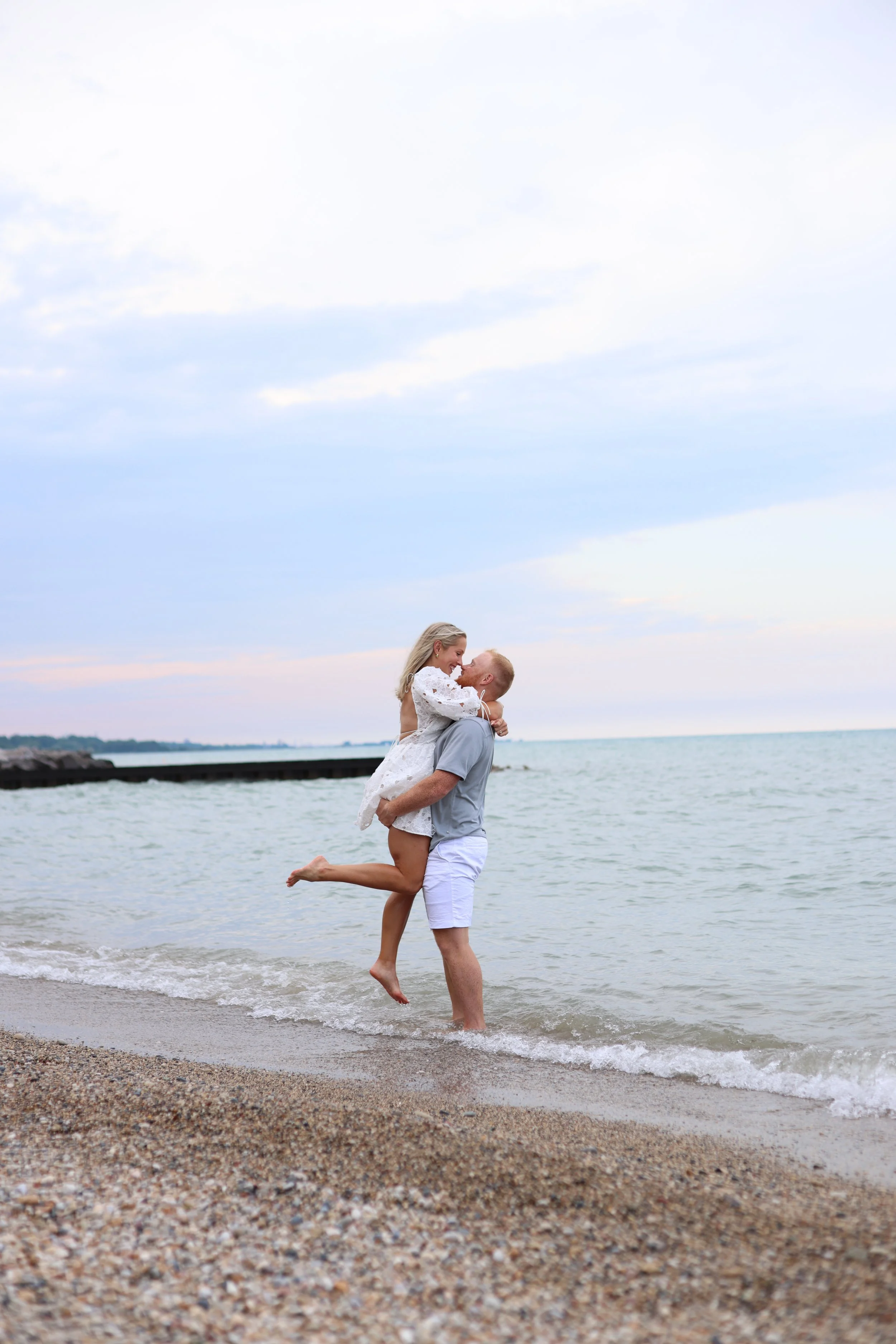 Couple embracing on a beach, man lifting woman, with ocean in background.