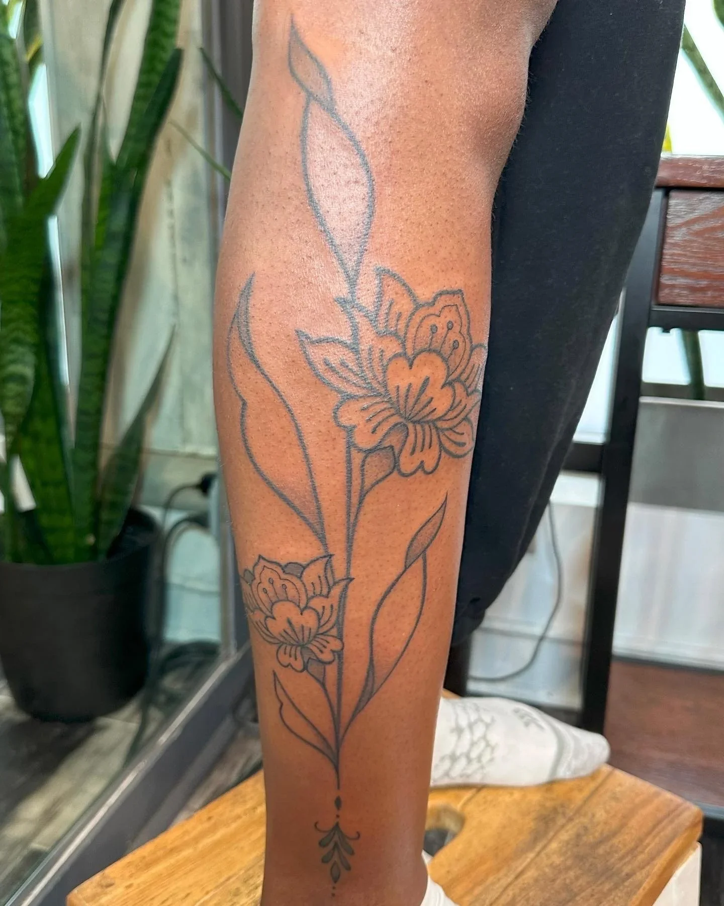 A person's forearm with a floral tattoo featuring a large flower and leaves, outlined in black ink.