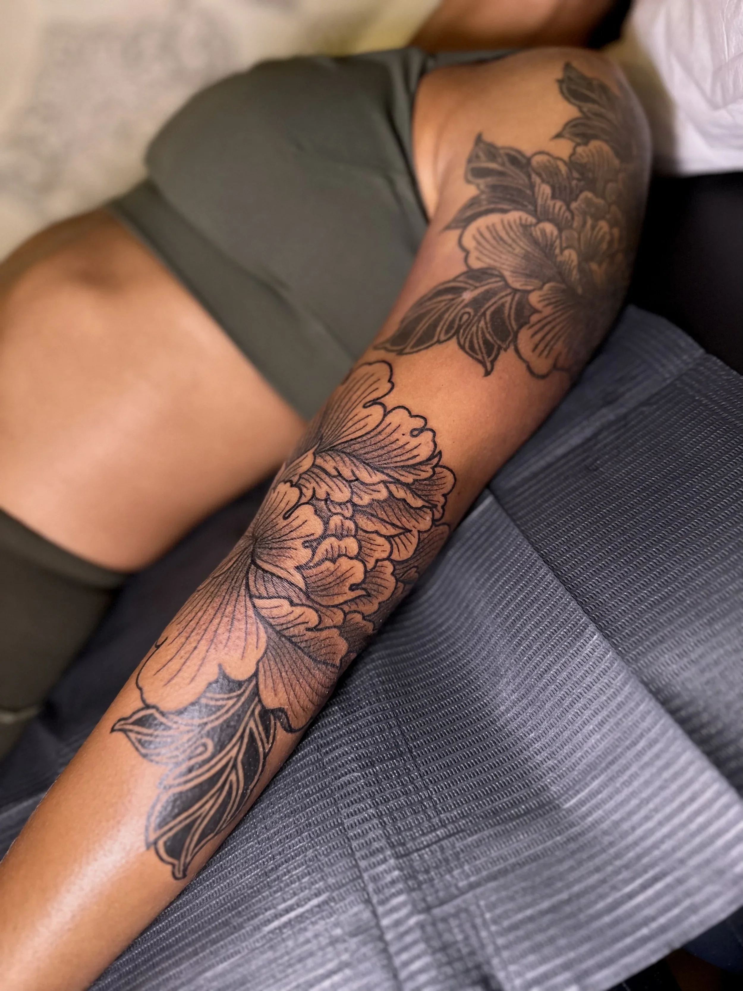Close-up of a person's arm with a detailed black floral tattoo and part of their gray shirt visible.