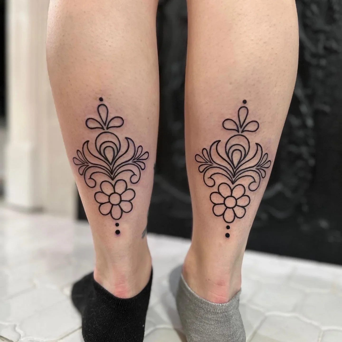 Matching floral tattoos on the lower legs of two people, one with black sock and the other with gray sock.