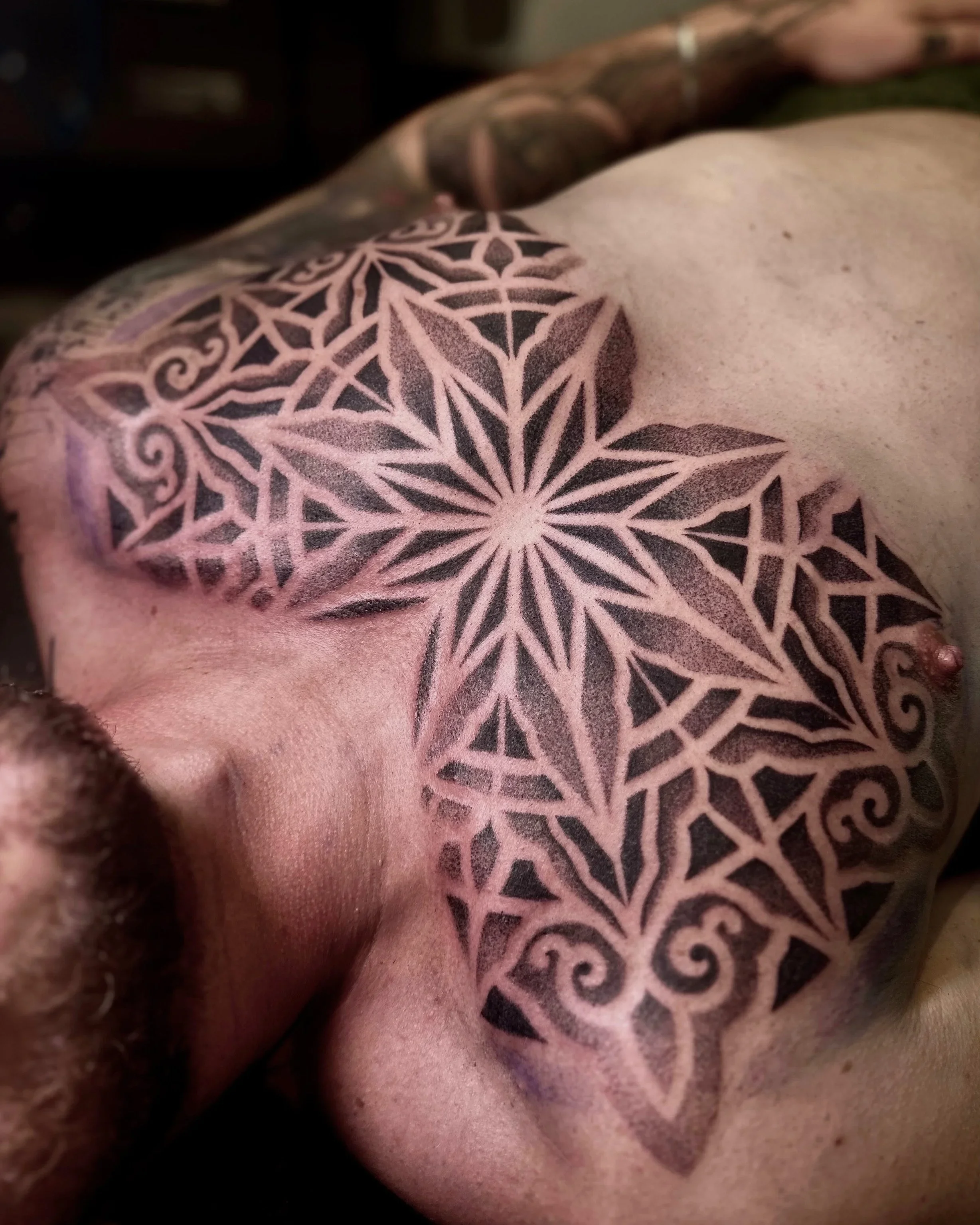 Close-up of a person's back with a large black and pink geometric tattoo design.