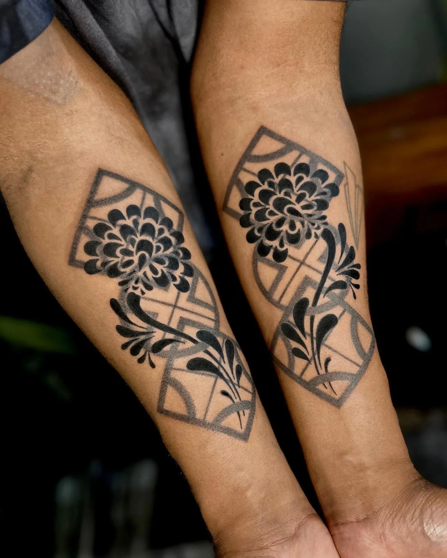 Close-up of a person's lower arms with black floral tattoos inside rectangular frames.