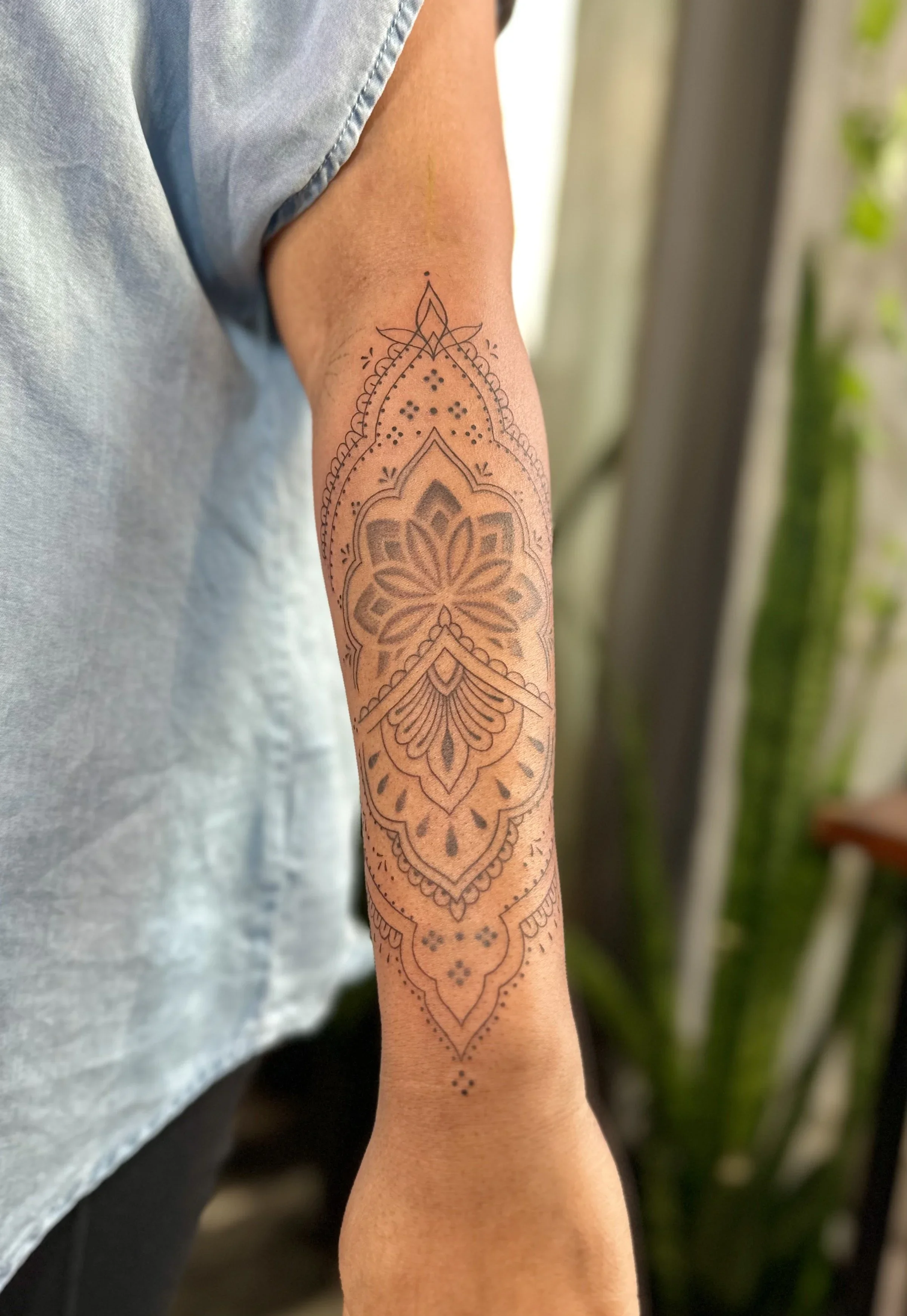 A tattoo on a person's arm features intricate geometric and floral patterns in black ink, with some shading and dot work.