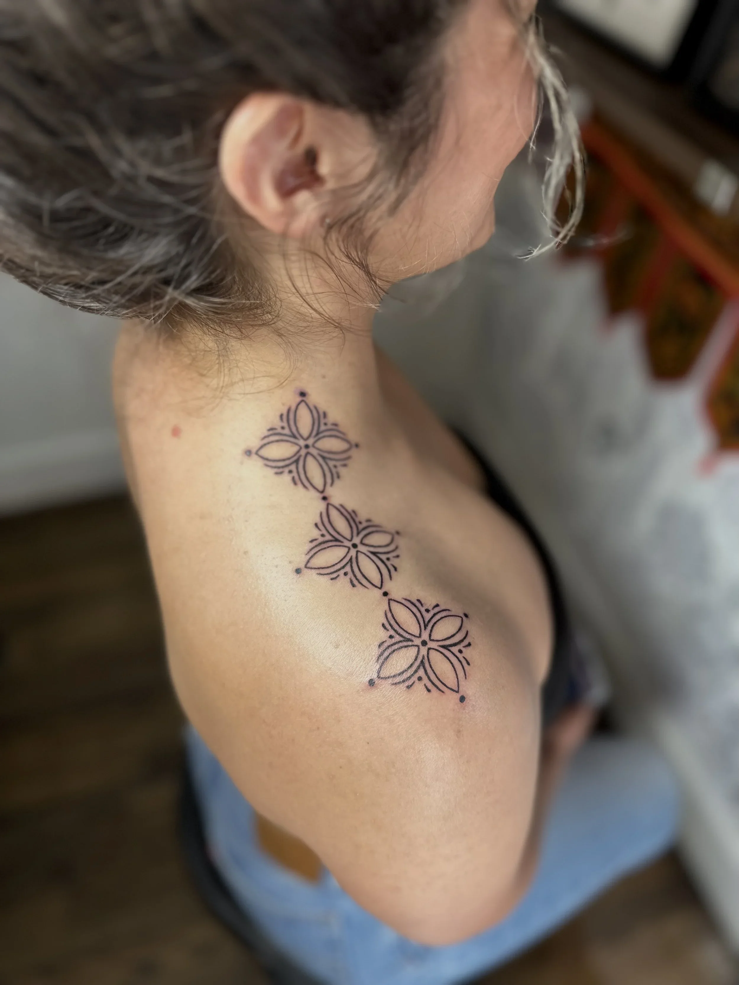 A close-up of a person's shoulder and upper arm with a temporary tattoo of a symmetrical floral pattern in dark ink.