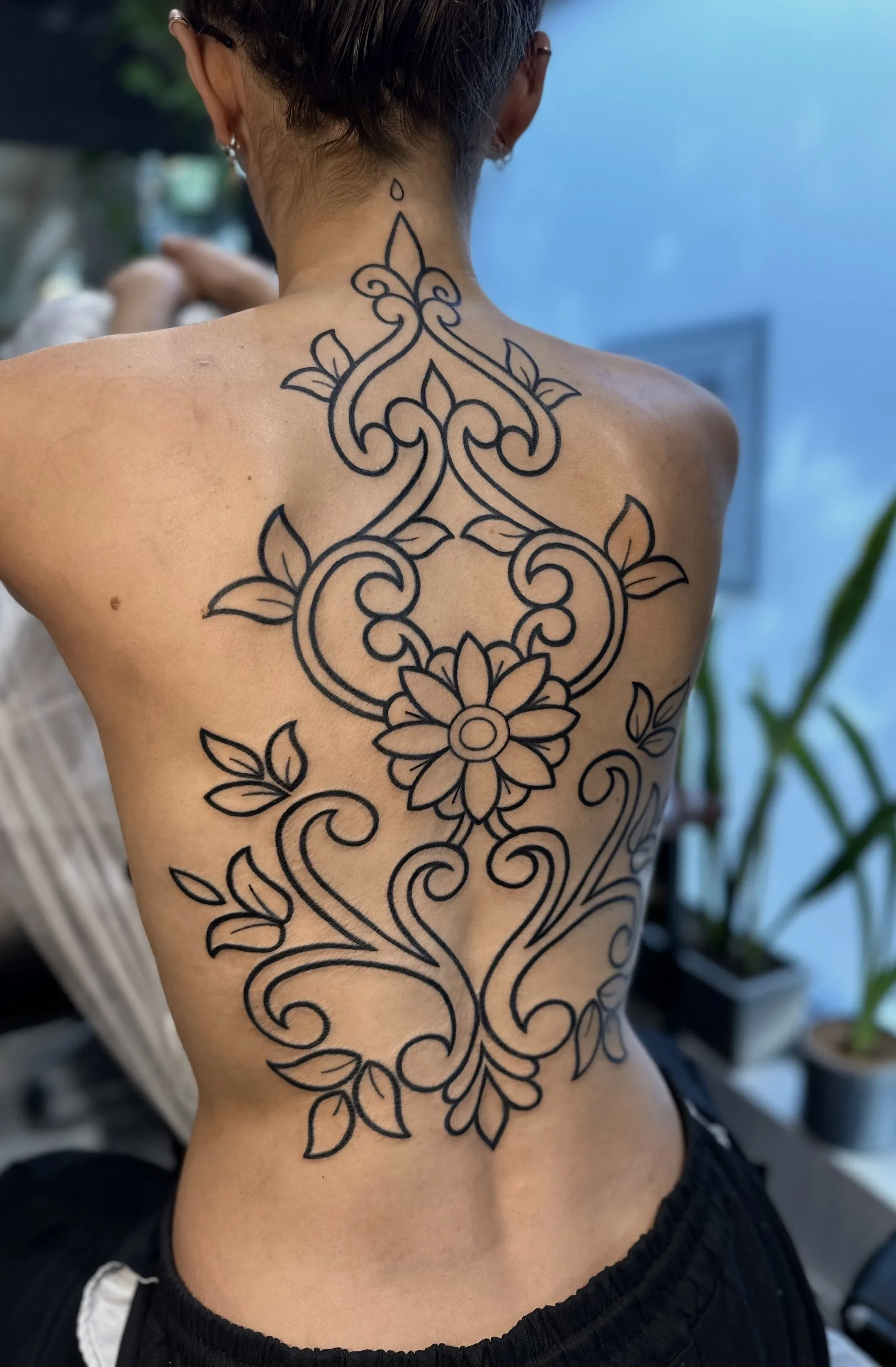 Back of a person's neck and shoulder with a large black outline floral tattoo.