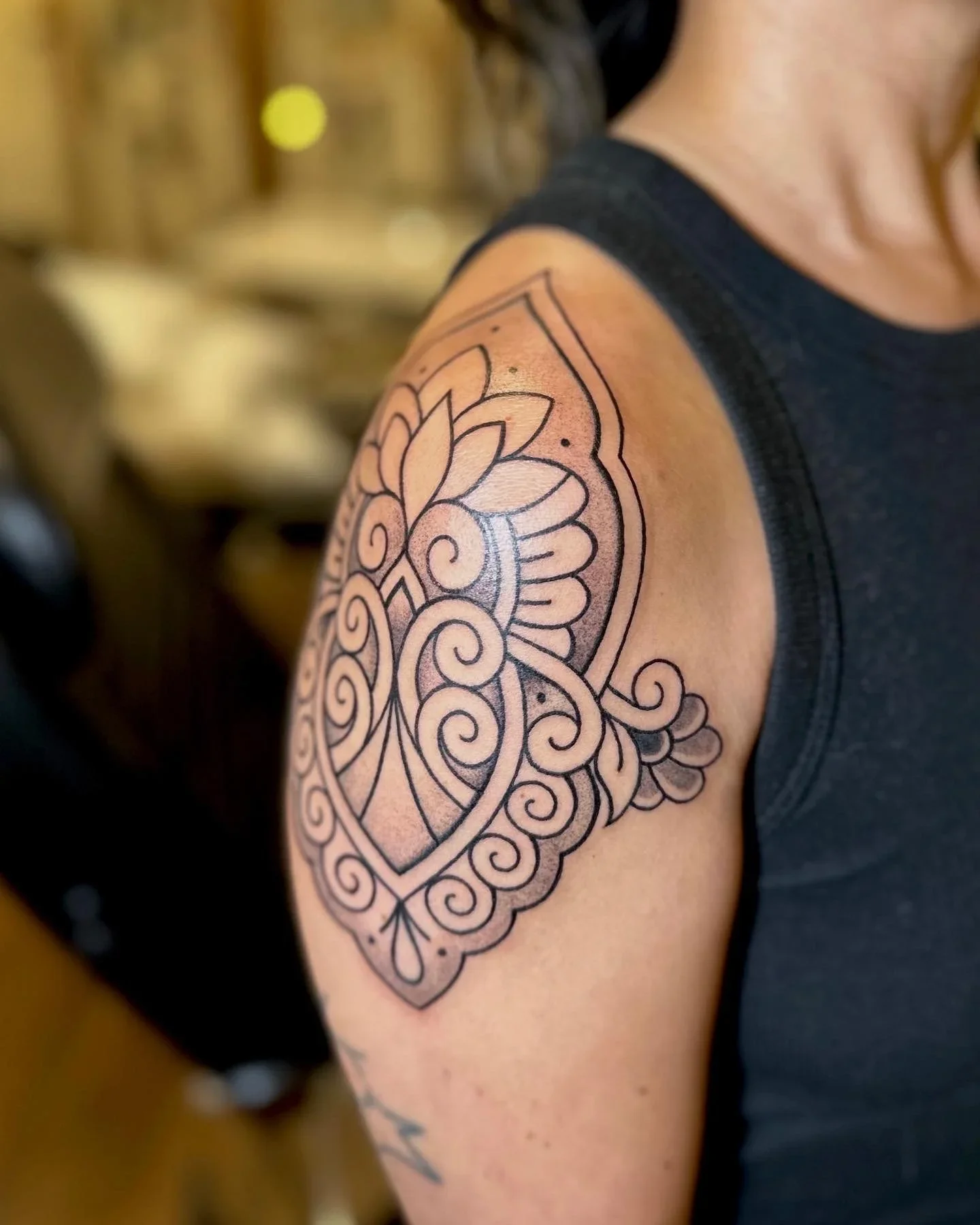 A close-up of a person's upper arm with a black outline tattoo featuring a intricate floral and mandala design.
