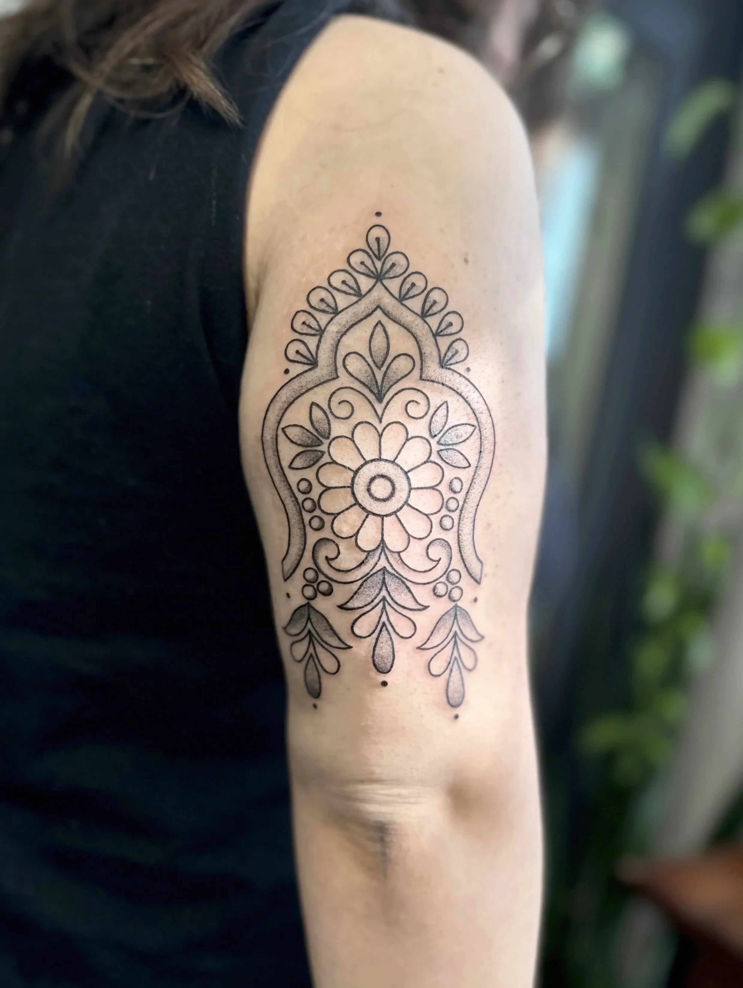 Close-up of a person's arm with a detailed, black outline tattoo of a floral mandala design.