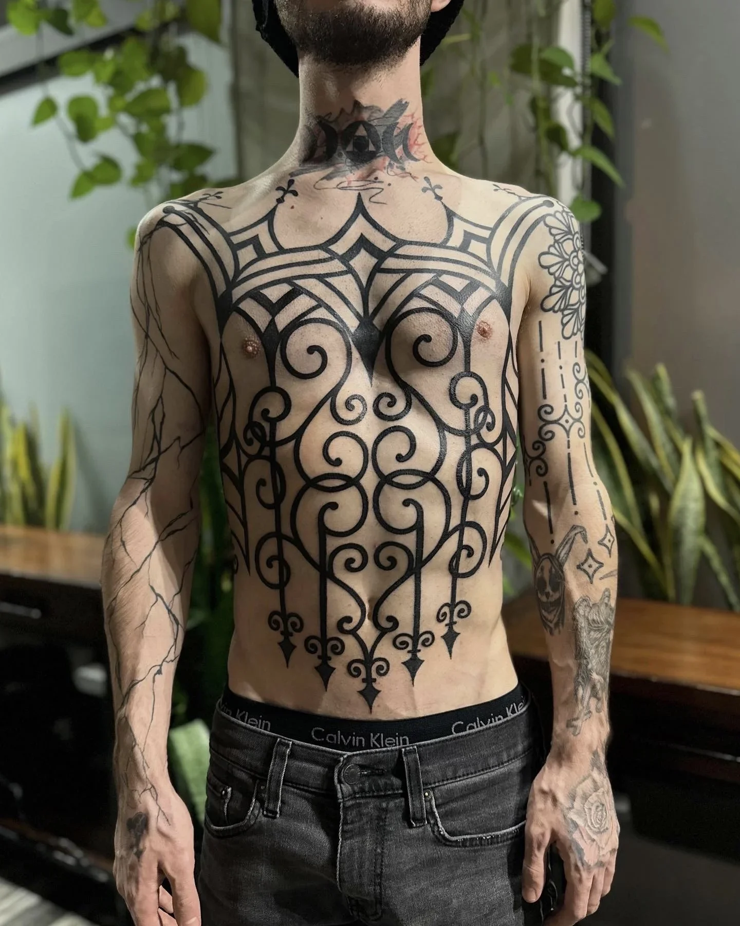 A shirtless man with extensive black tattoos covering his chest, arms, and neck.