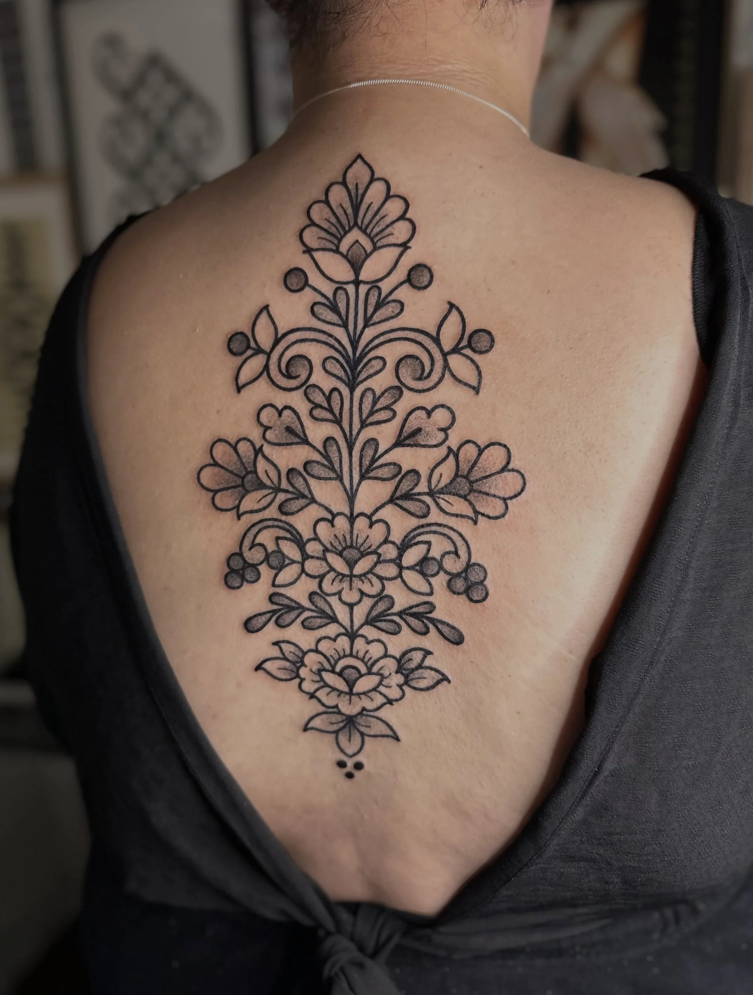 A person with a tattoo of a symmetrical floral and leaf design running down their back from the neck to the top of the waist.