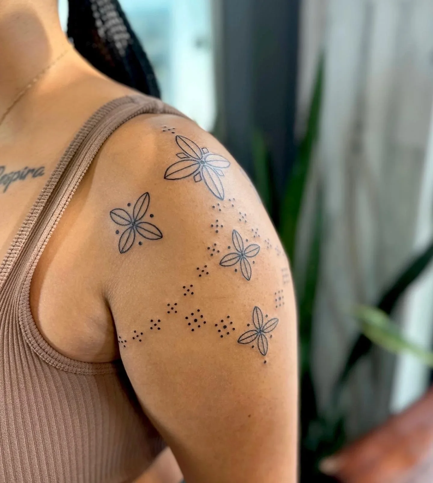 Tattoo of flowers and dotted patterns on a person's upper arm and shoulder.
