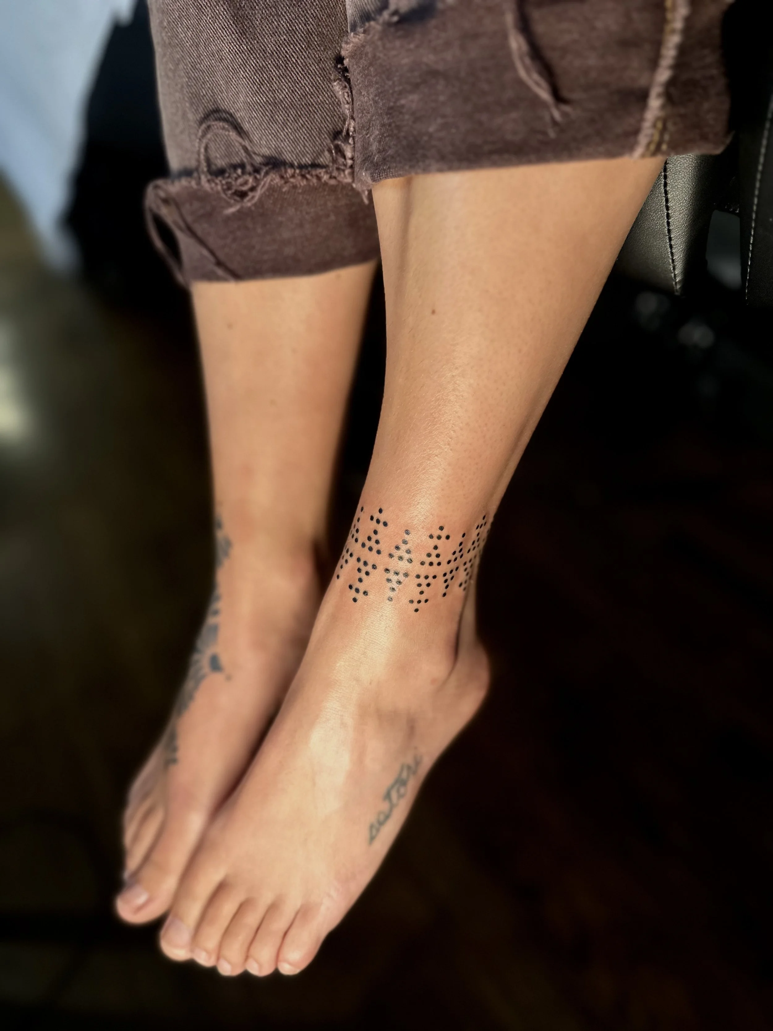 Close-up of a person's hand and forearm, wearing sheer black stockings with a dotted pattern near the toes, and a brown torn garment or blanket draped over the arm.