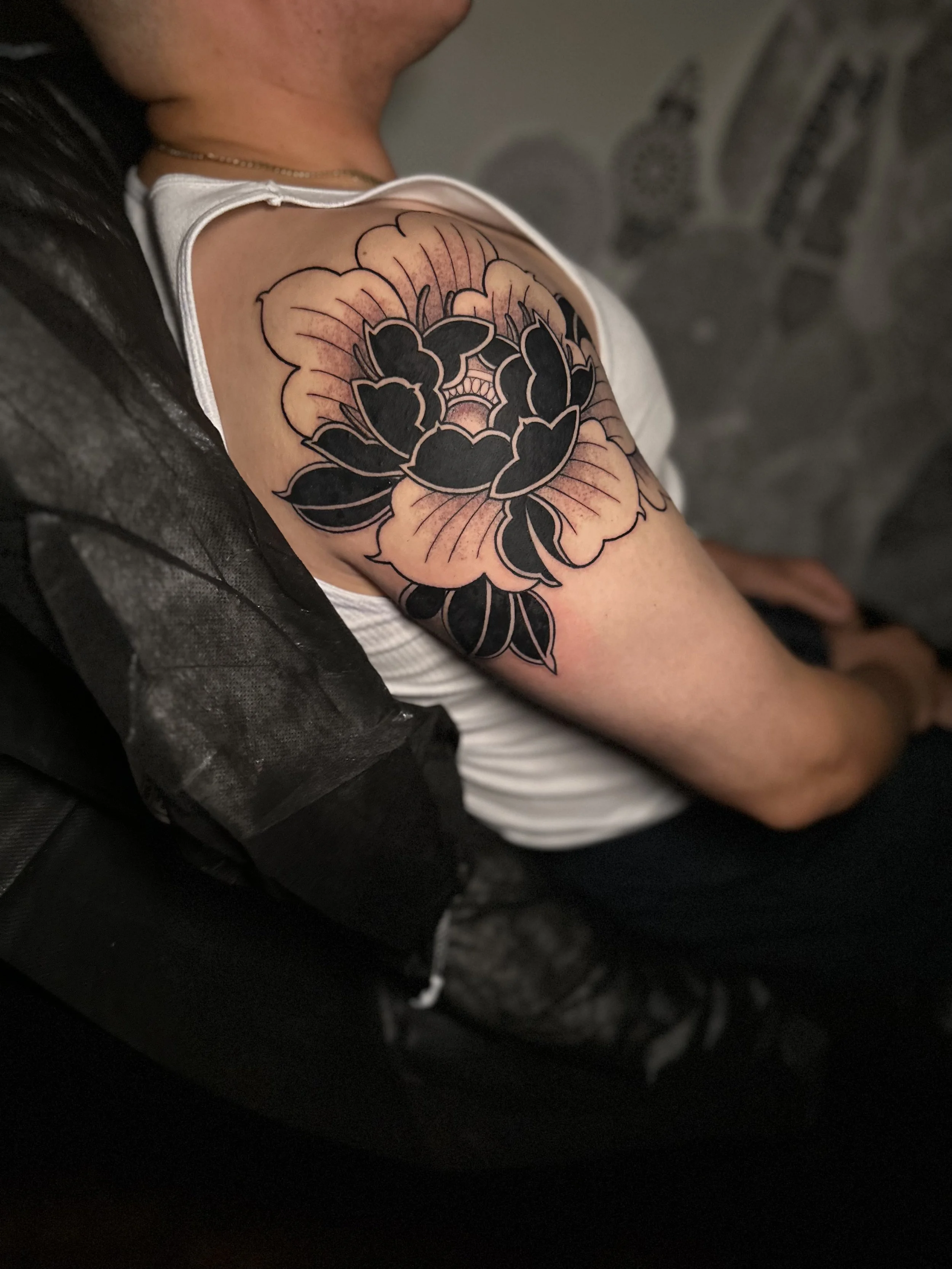 A close-up of a person's upper arm with a large floral tattoo featuring dark leaves and pinkish petals.