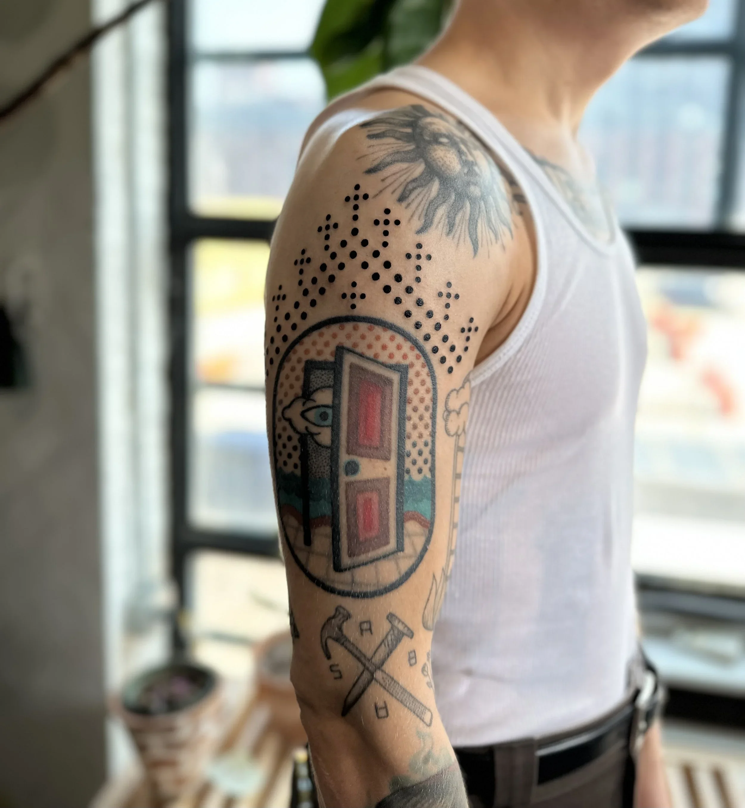 A person's arm with a tattoo of a lion's head and an abstract geometric design, including dots and a compass, on the upper arm, in an indoor setting.