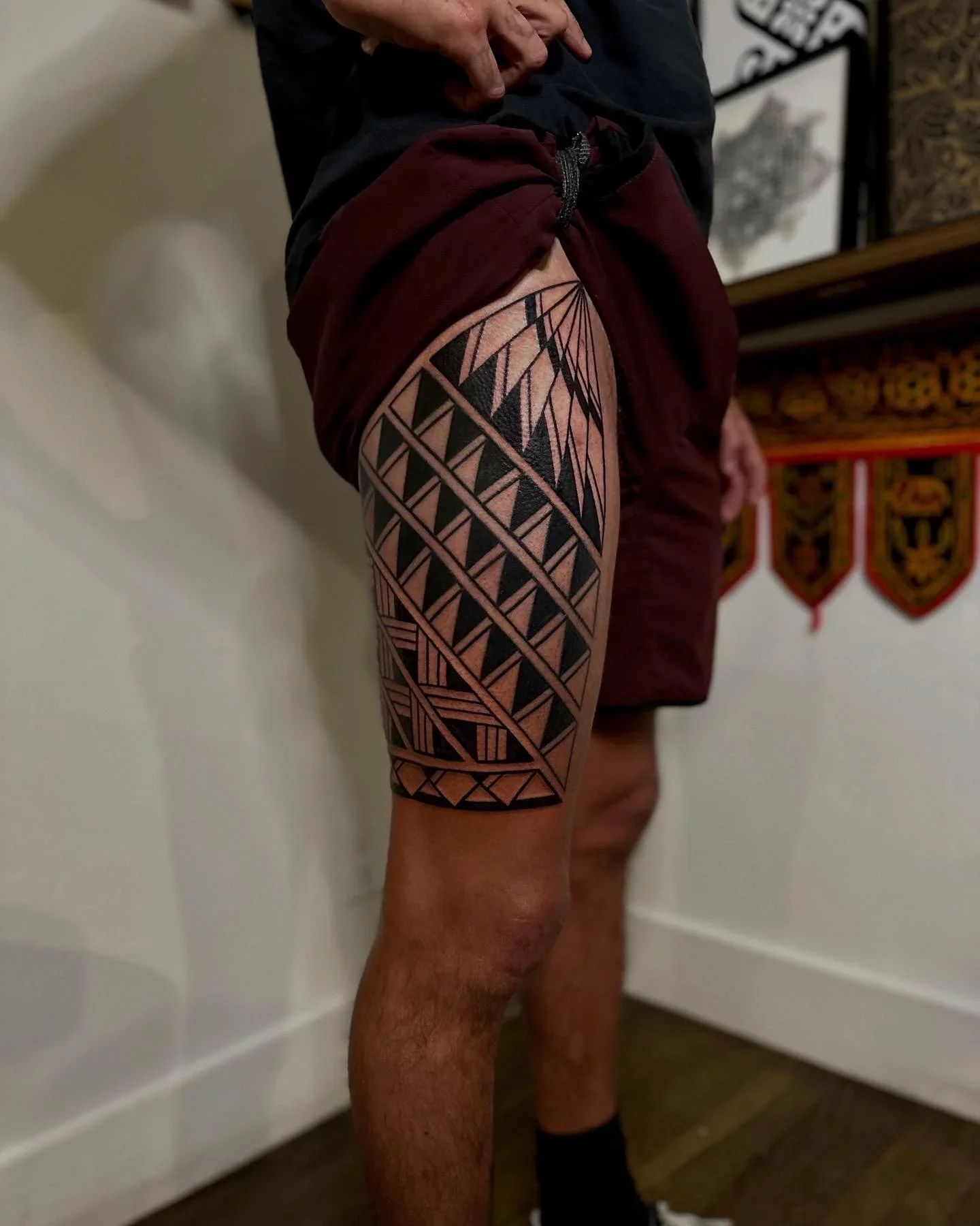 A person's upper leg features a large geometric tattoo with black lines and shapes, including triangles and diamonds, covering the thigh area.
