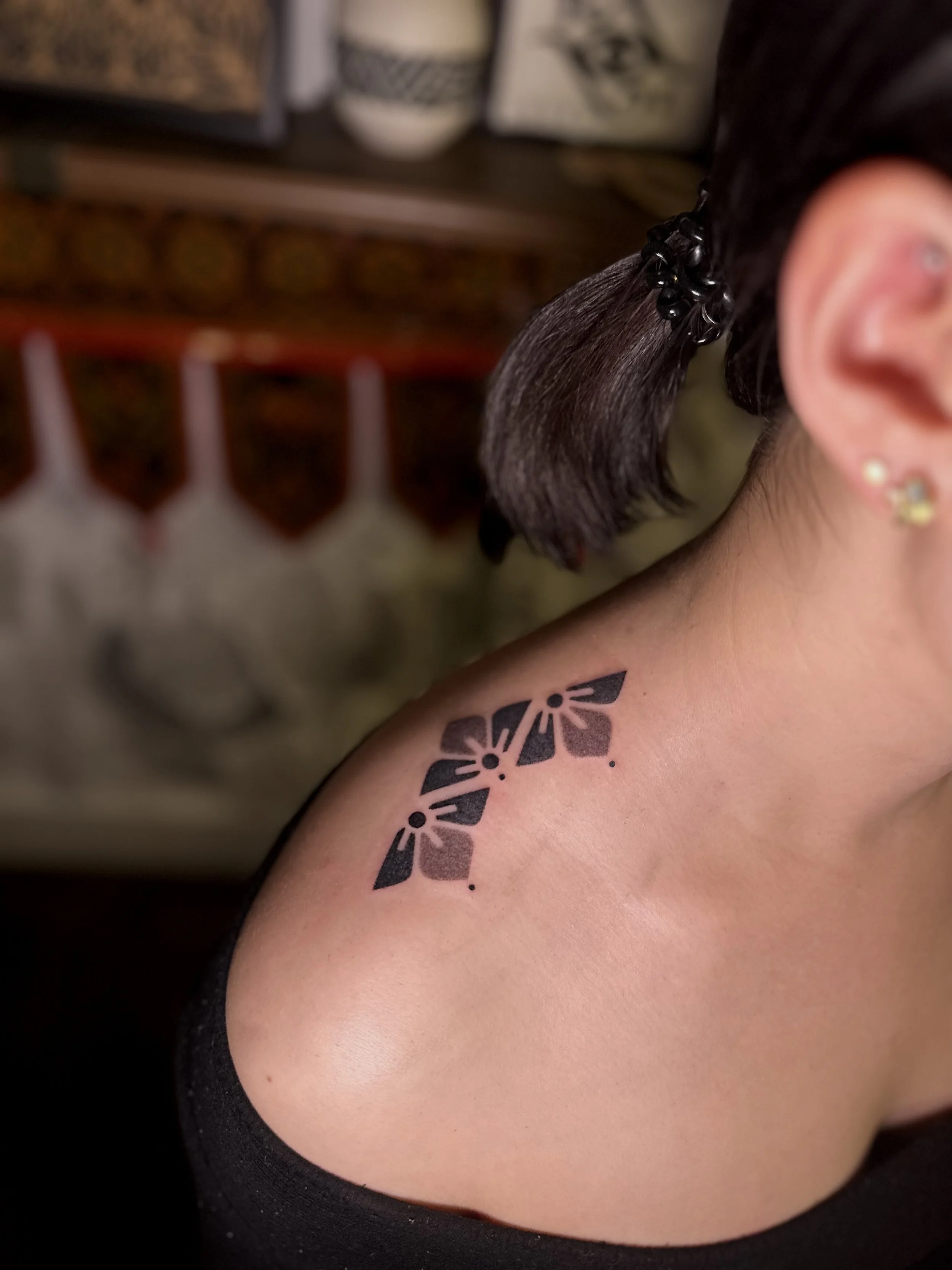 Close-up of a person's shoulder with a black butterfly tattoo, part of an earring, and their brown hair tied with a black hair accessory.