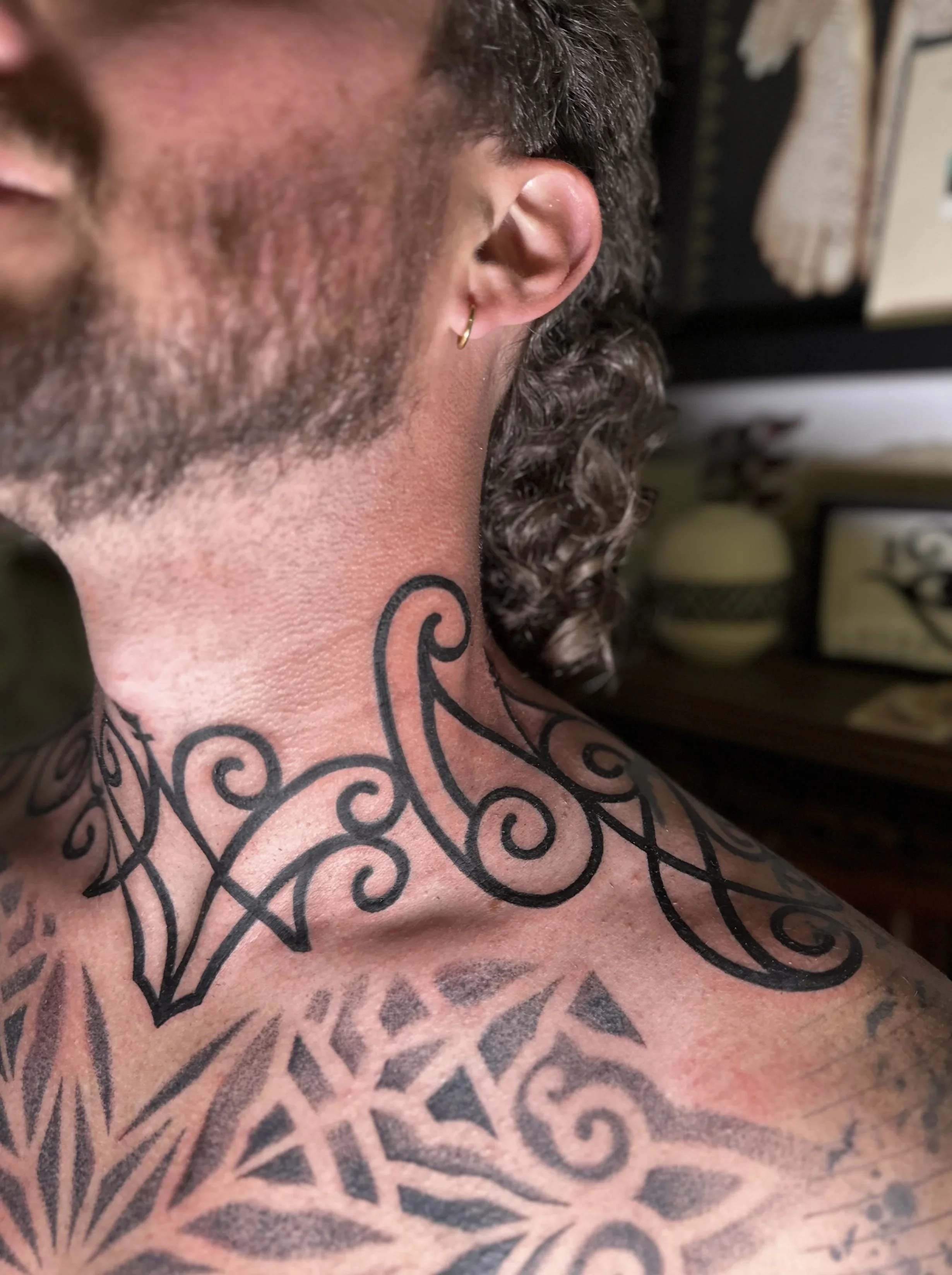 Close-up of a person's neck and shoulder, showing tattoos and a gold hoop earring in the ear.