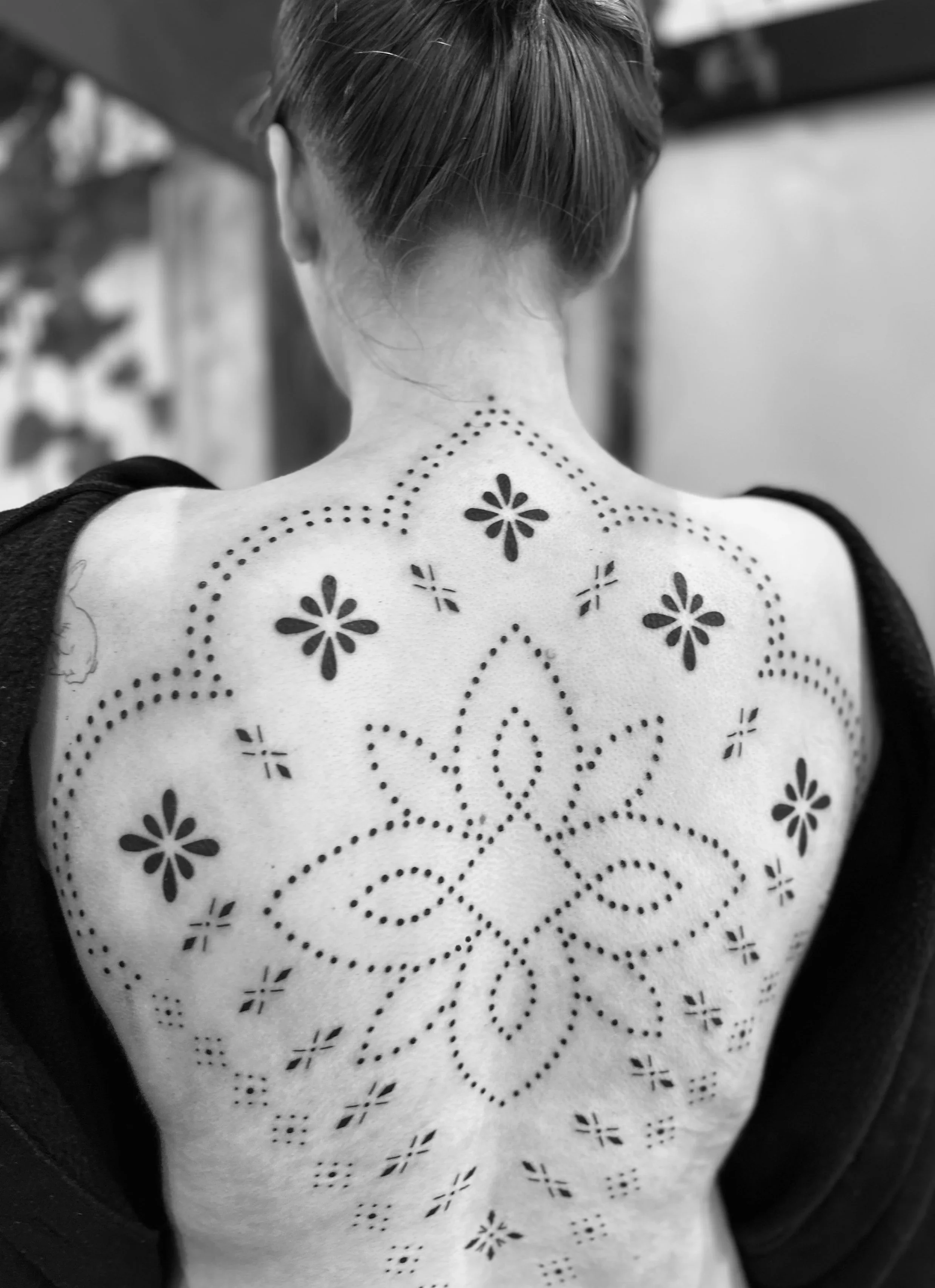 Back of a woman's neck and upper back with floral and dotted tattoo designs.