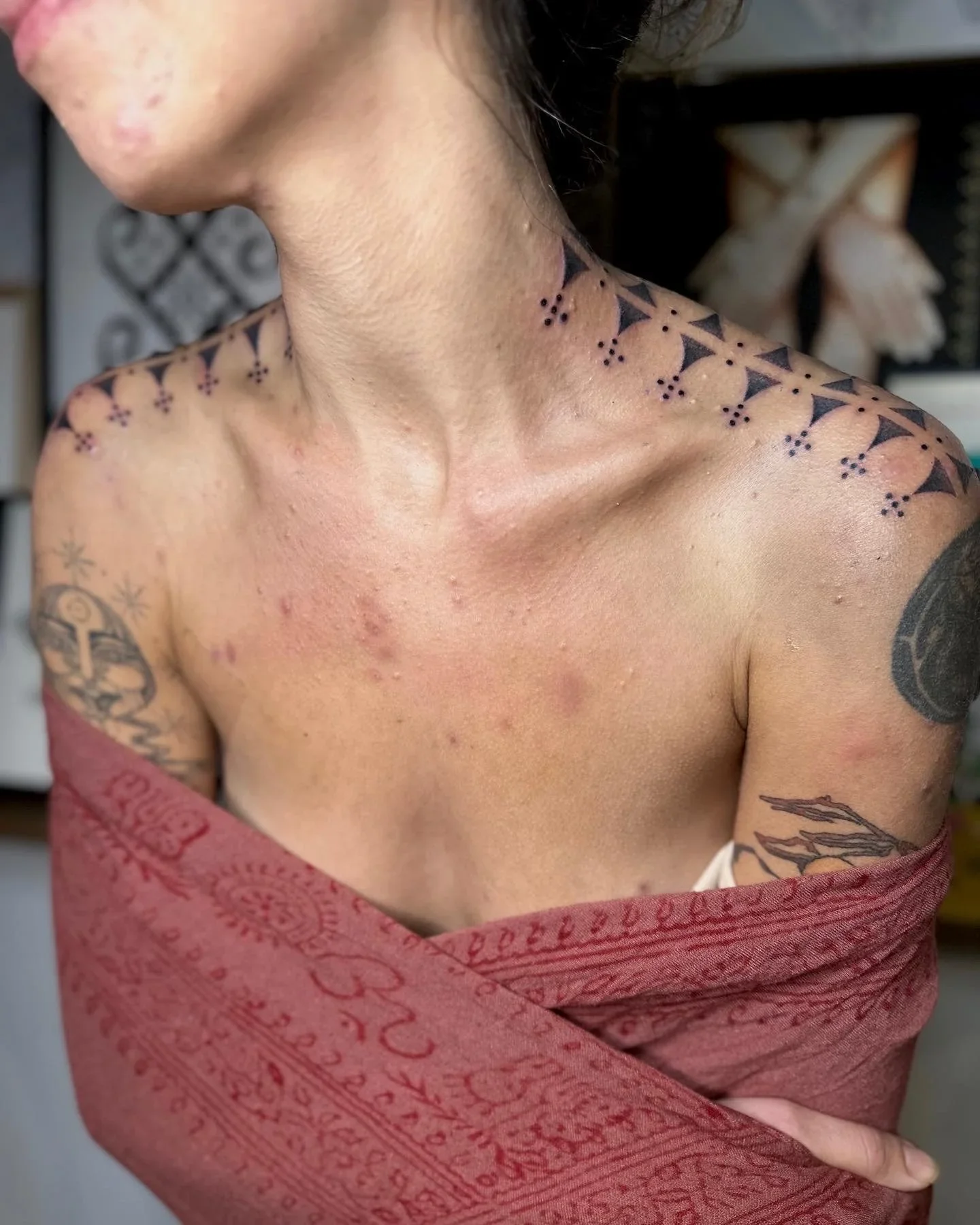 Close-up of a person's shoulder and neck area with tattoos, partially wrapped in a red patterned cloth or towel.