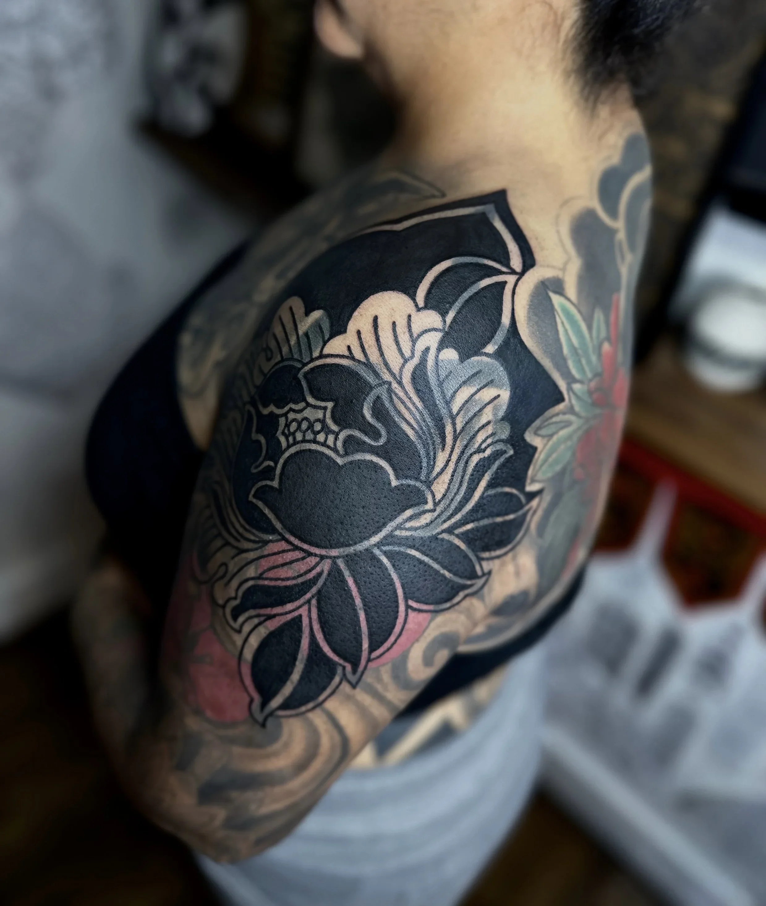 Close-up of a tattoo on a person's shoulder, featuring a detailed flower design in black and grey ink.