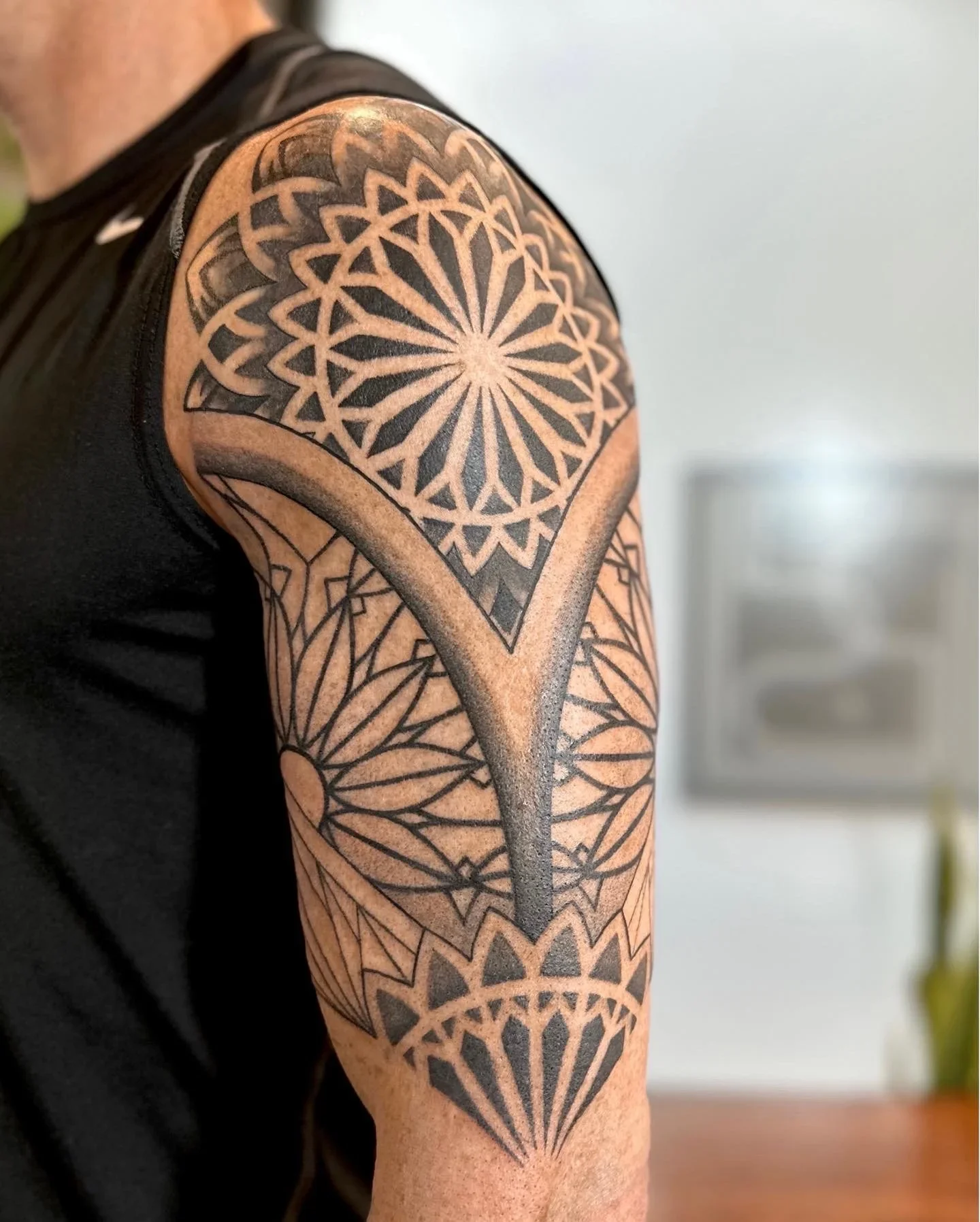 Close-up of a person's shoulder with a geometric black tattoo design covering the upper arm and shoulder.