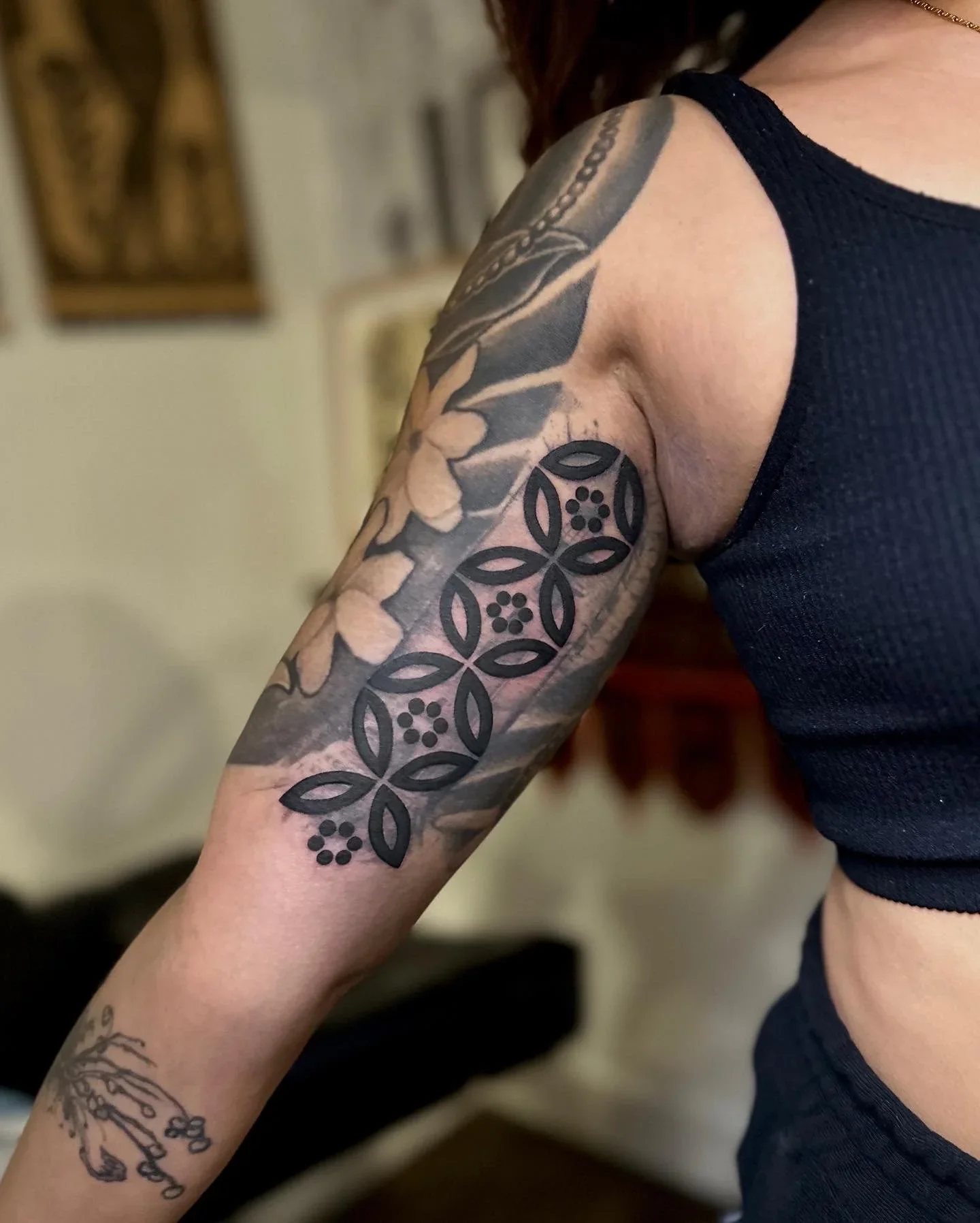 Close-up of a person's arm with a black floral tattoo sleeve, wearing a sleeveless black shirt.