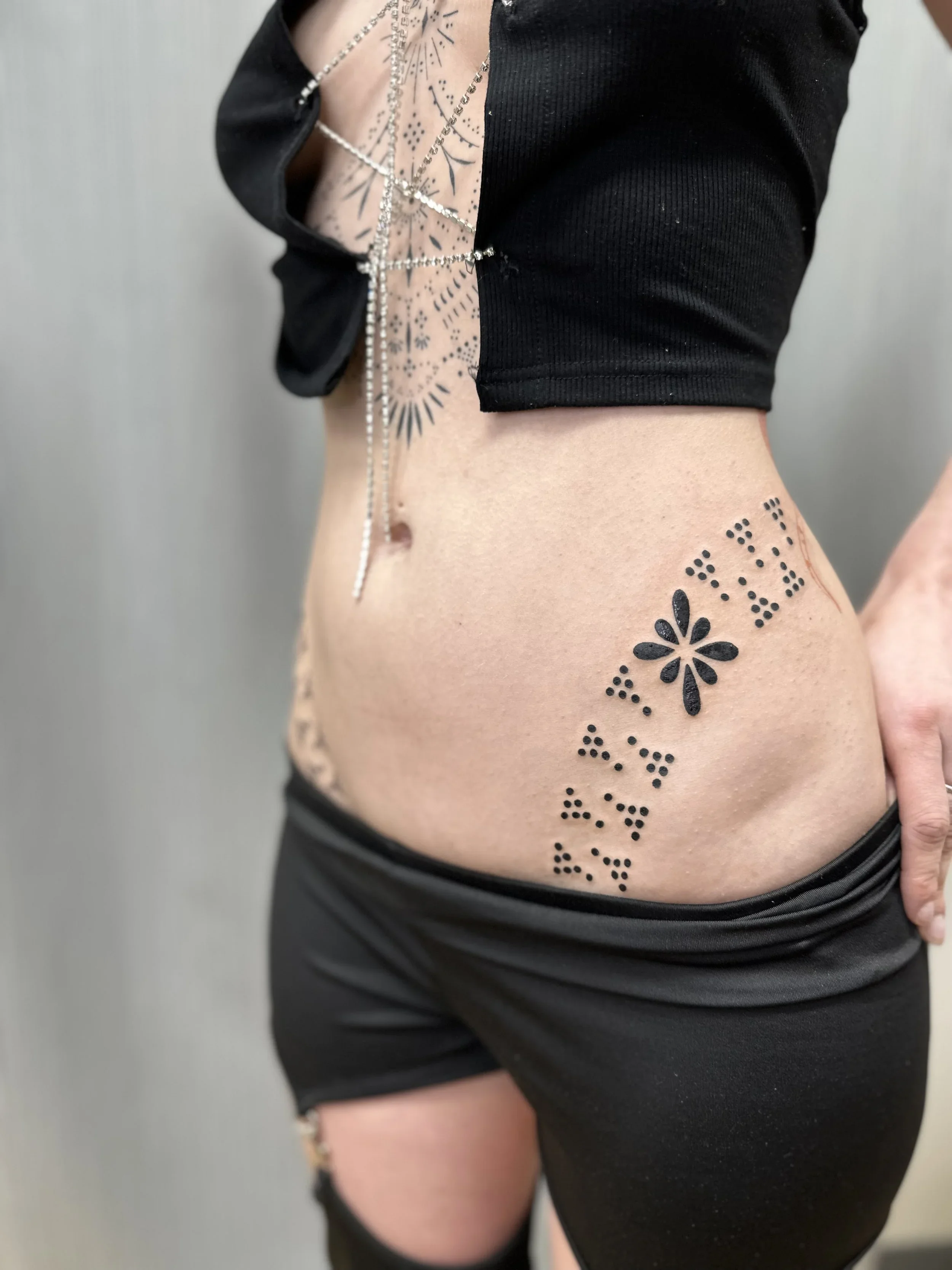 A person's side torso and upper arm, with tattoos and jewelry visible, wearing a black top and black shorts.