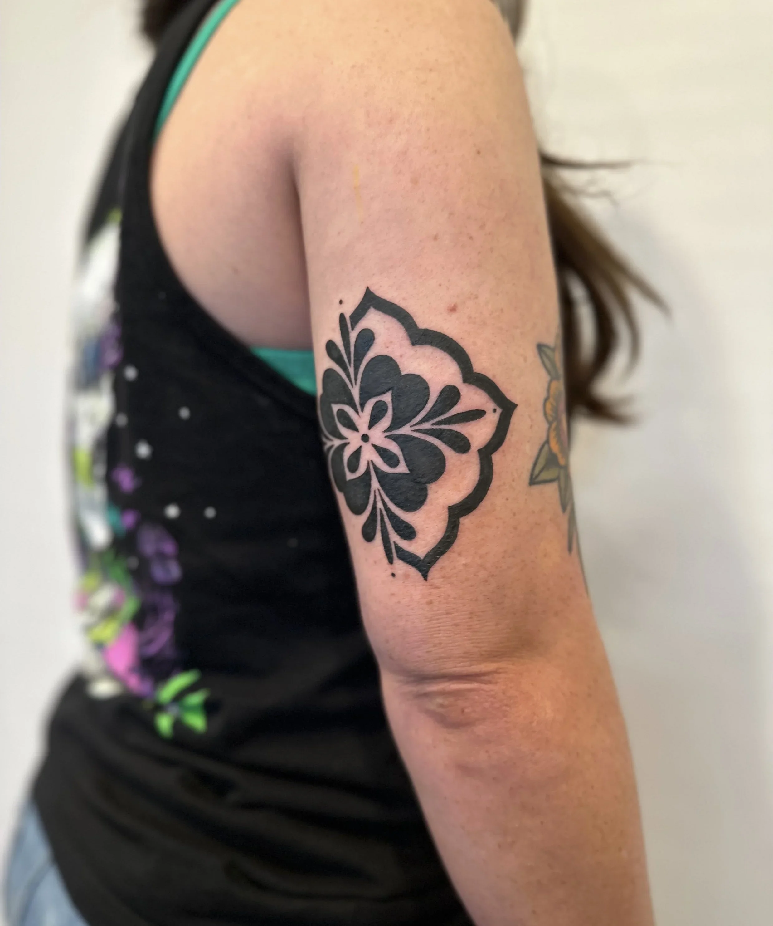 Close-up of a person's upper arm and shoulder, showing a black ink floral tattoo on their upper arm.