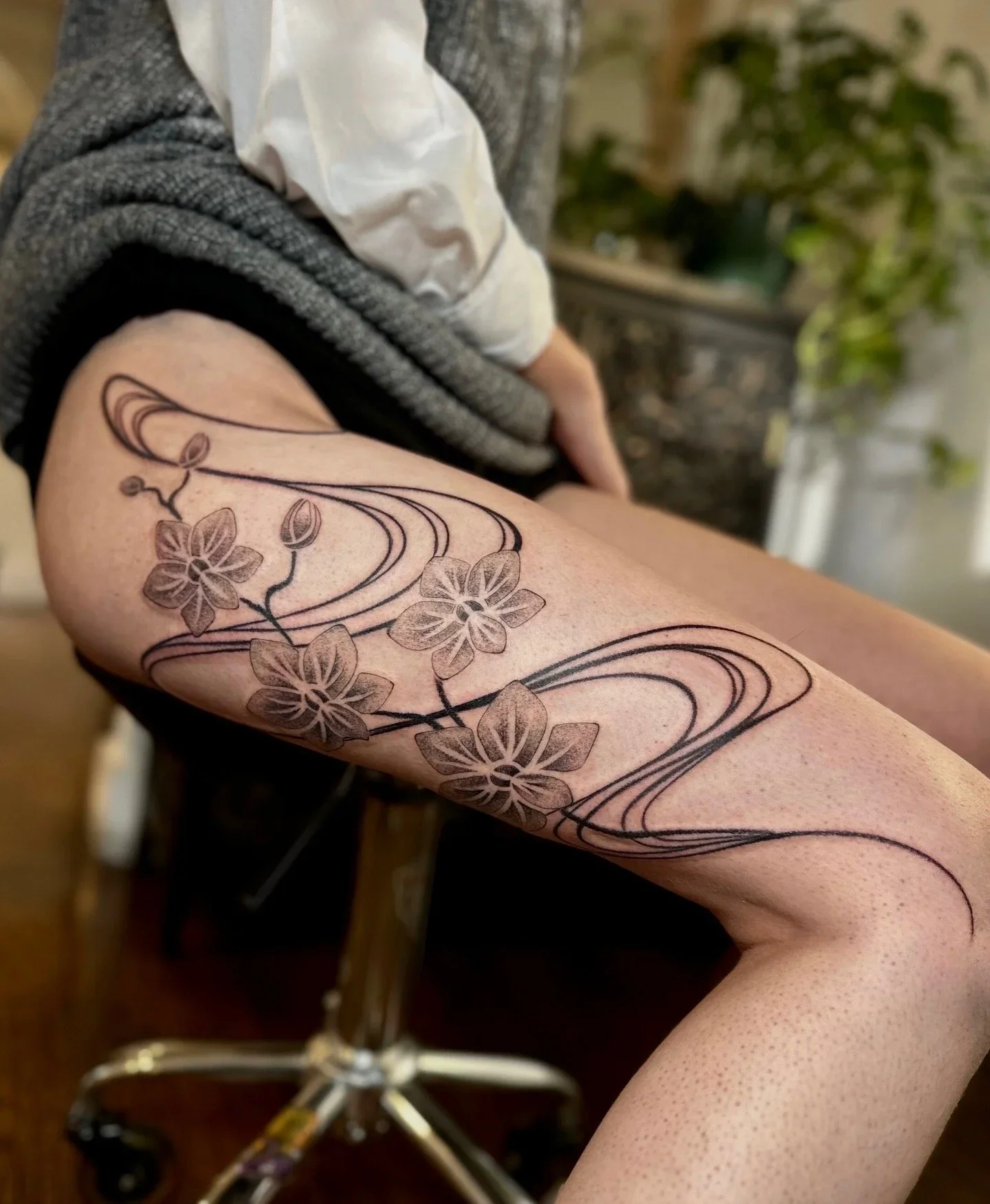 A person's arm with a black and gray floral tattoo featuring flowers and swirling lines.