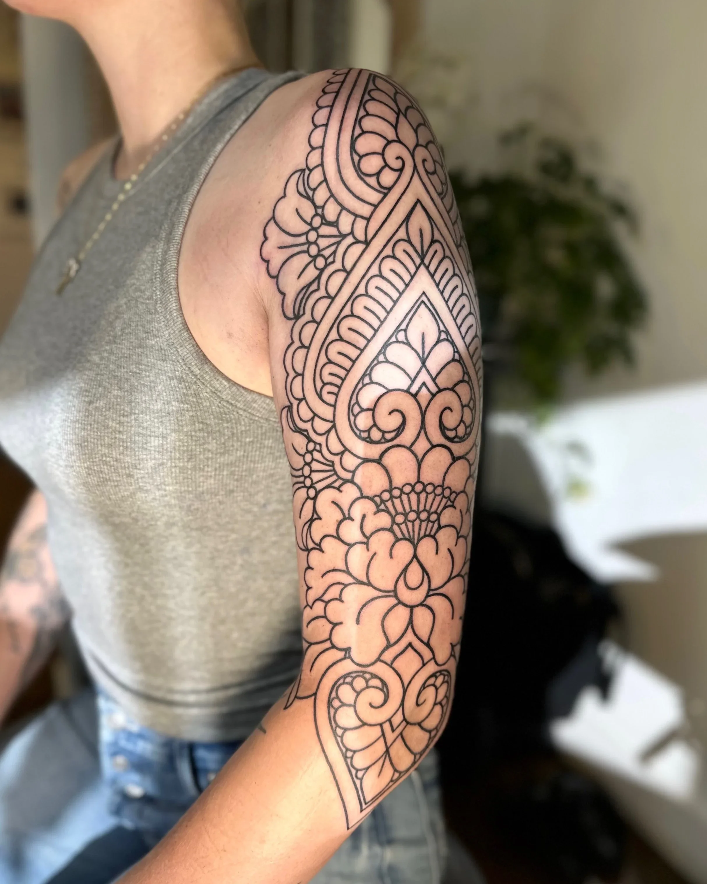 A person with a tattoo sleeve on their upper arm featuring intricate, black line patterns and floral designs.