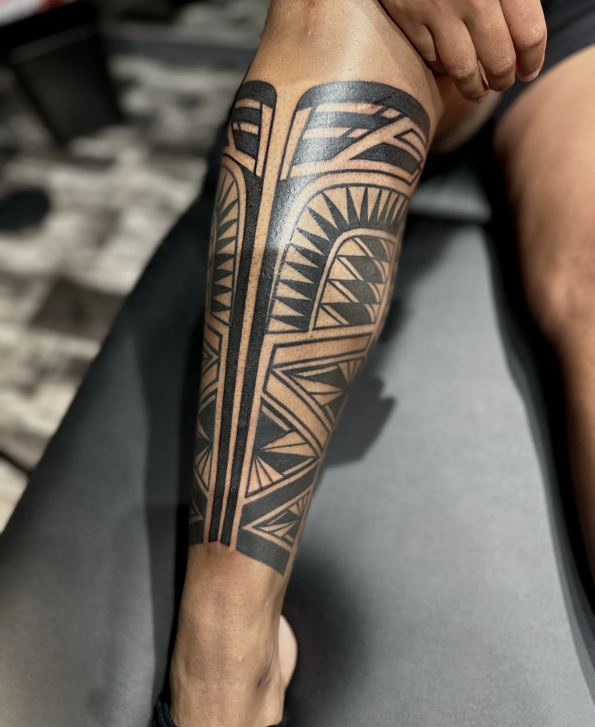 Close-up of a person's leg with a black geometric tattoo covering part of the calf.