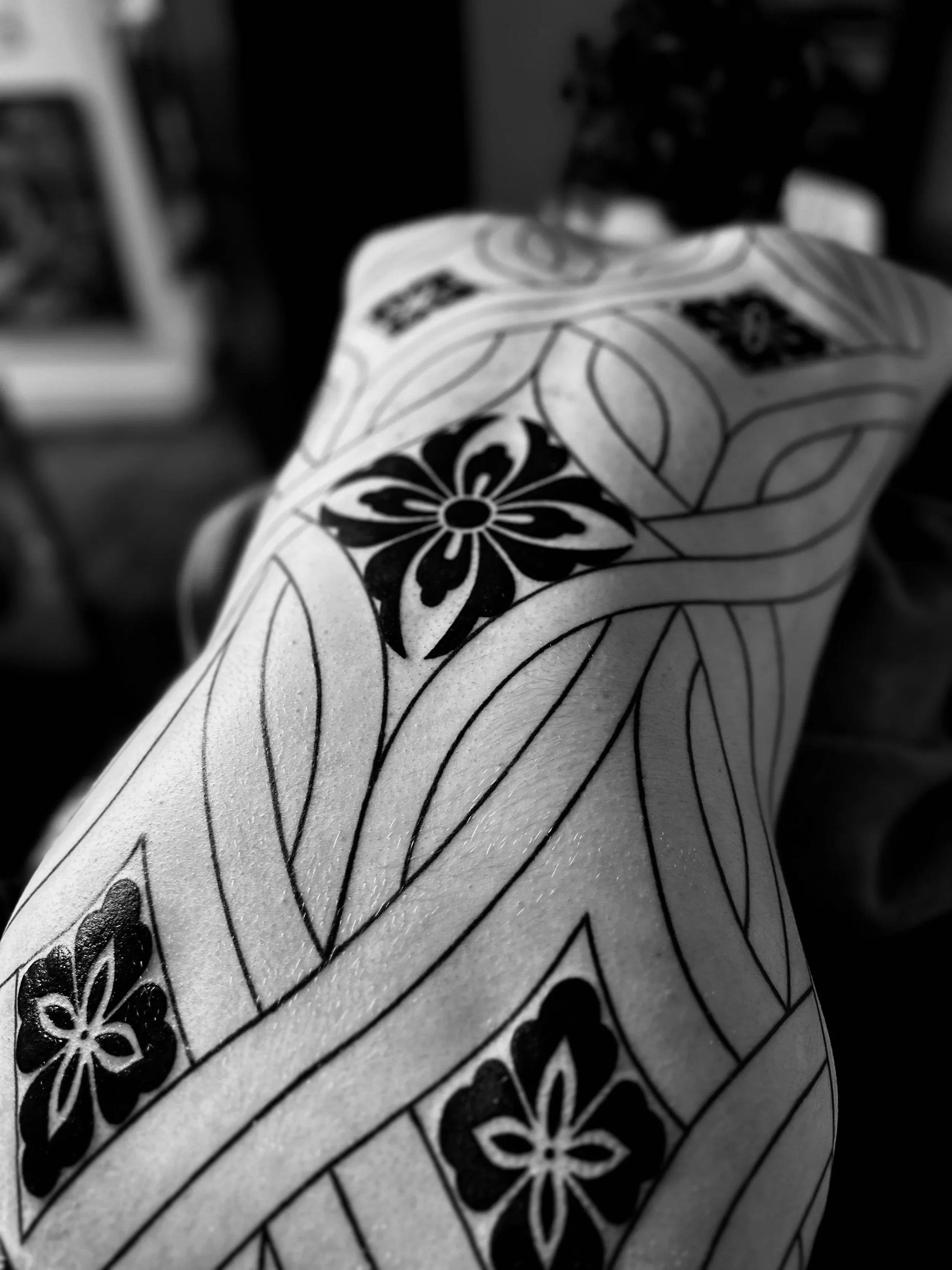 Close-up of a person's arm with a tattoo featuring a large floral design, black and white color, with visible lines and patterns.